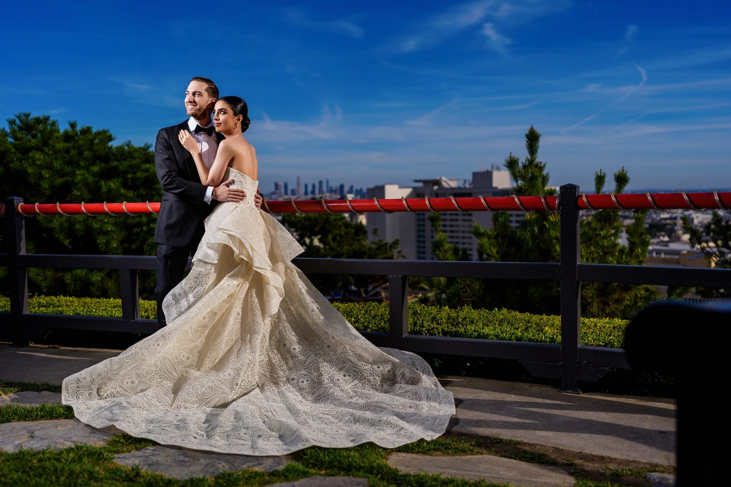 The bride leans back into the groom's embrace, her patterned train fanned wide across the walkway.