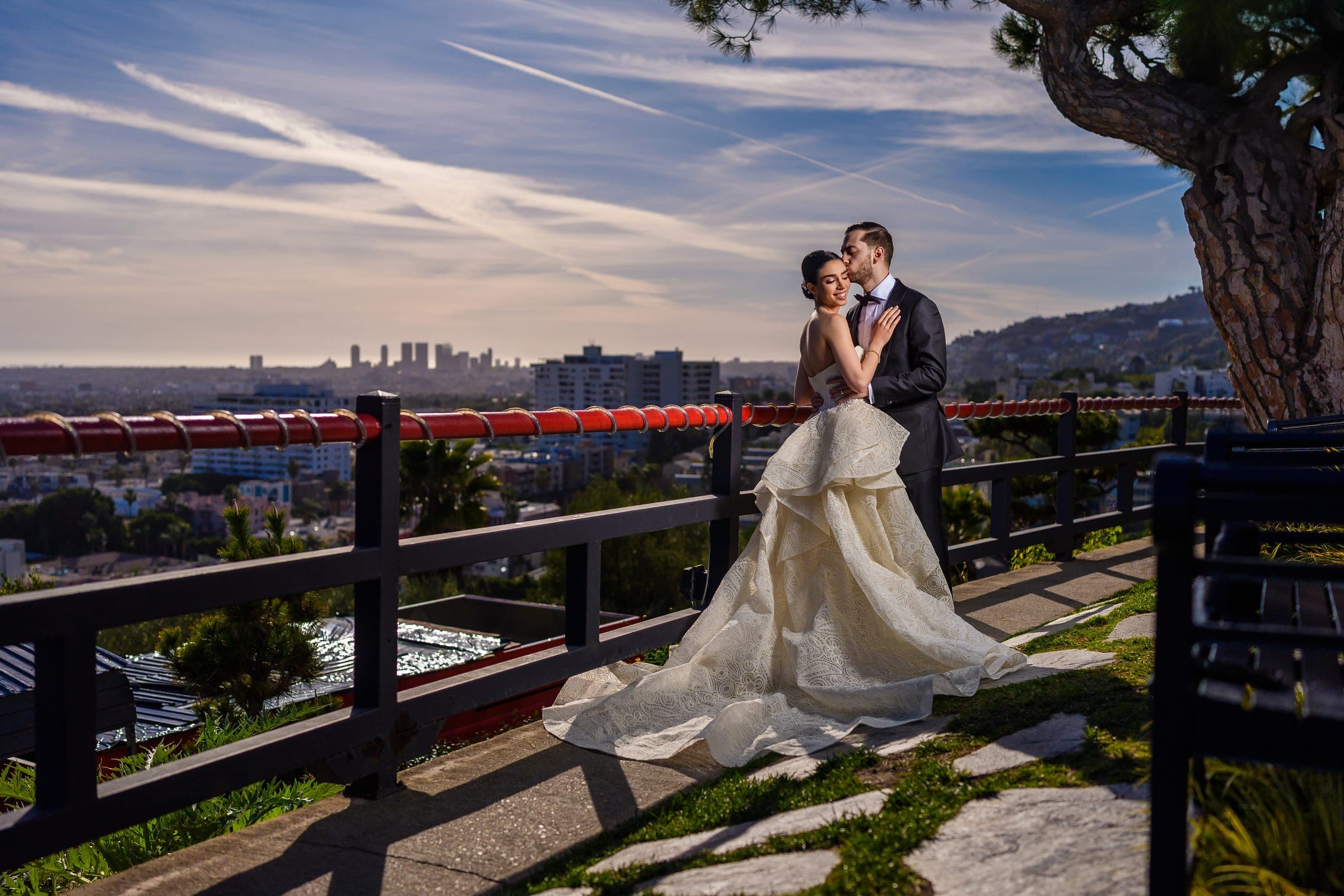 The couple embraces on a terrace walkway high above the city, her lace train trailing across the stones.