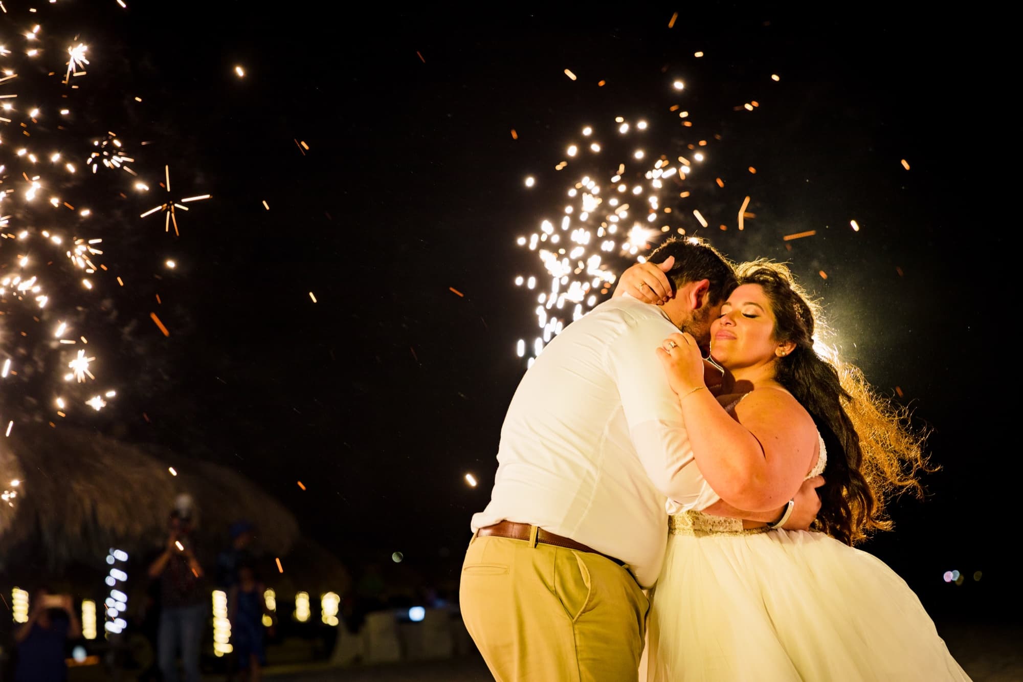Nikole and Nick kissing on the beach in a shower of sparkler light at night in Aruba