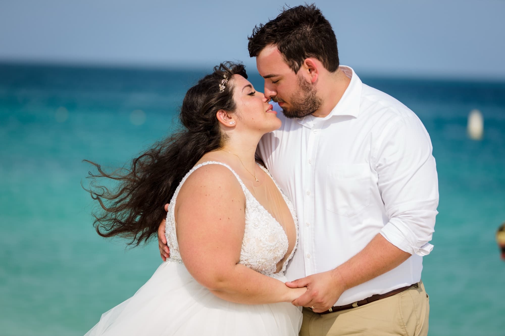 Close portrait of Nikole and Nick kissing with the bright turquoise Caribbean water behind them