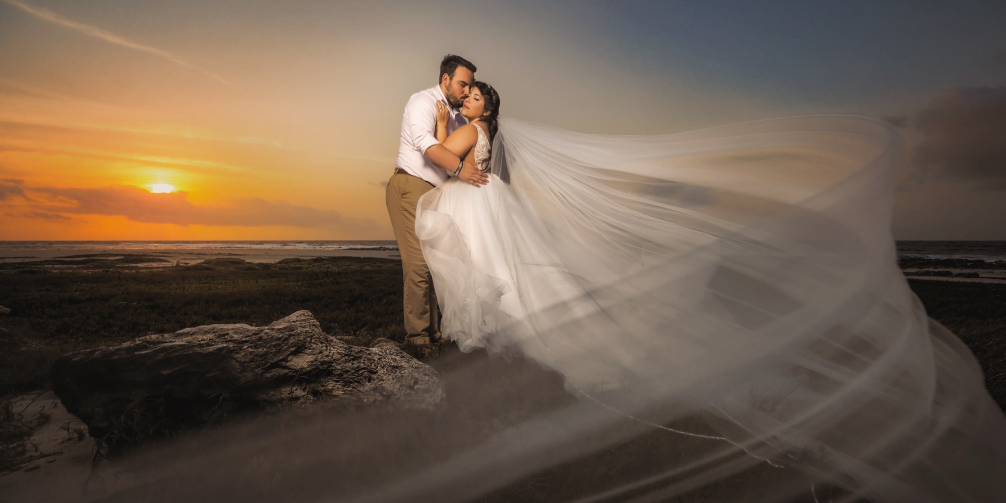 Nikole and Nick embracing beside the ocean at sunset in Aruba