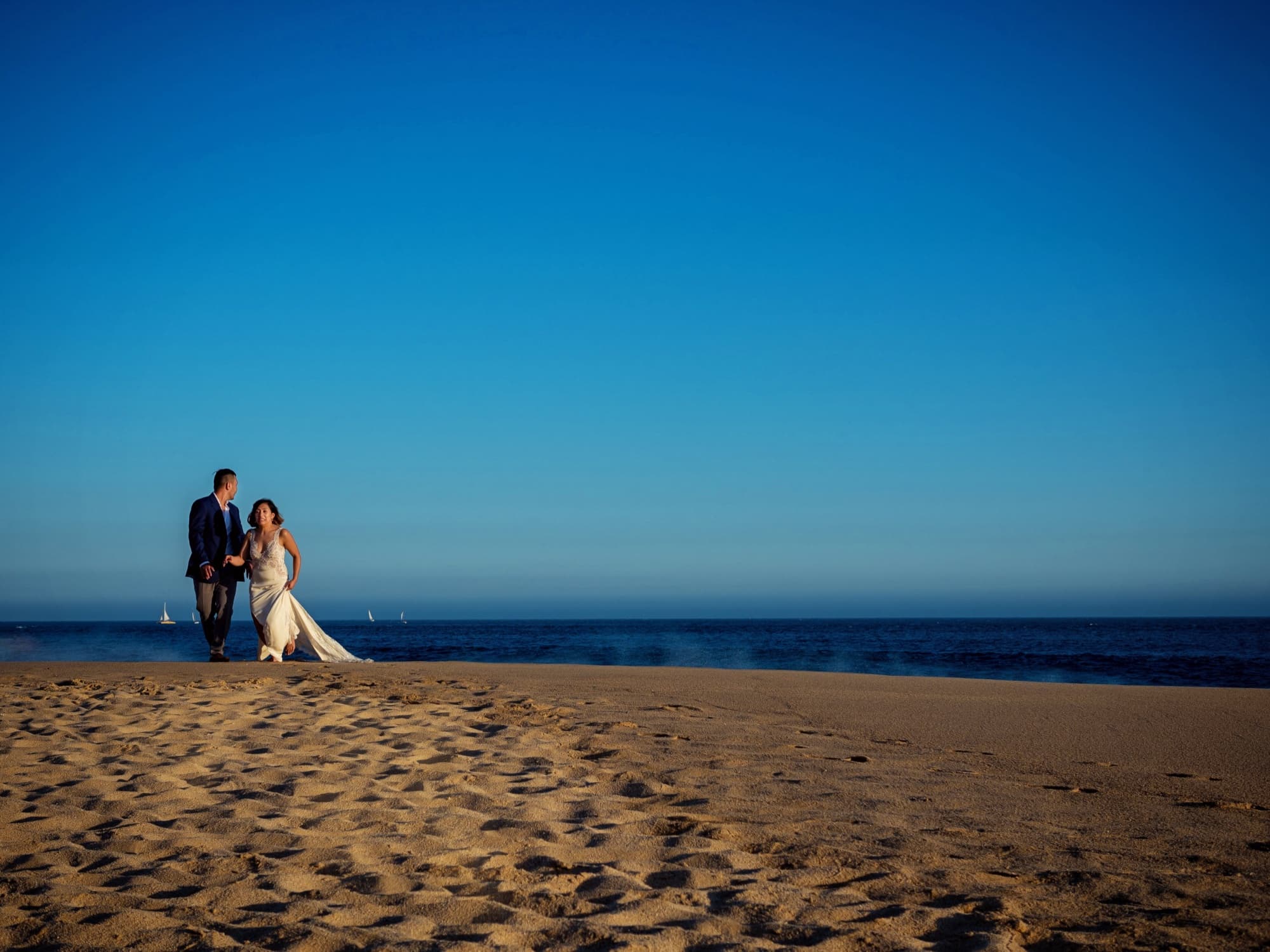 Kirsten and Jolan walking together on the beach in Cabo with a deep blue sea and sky behind them