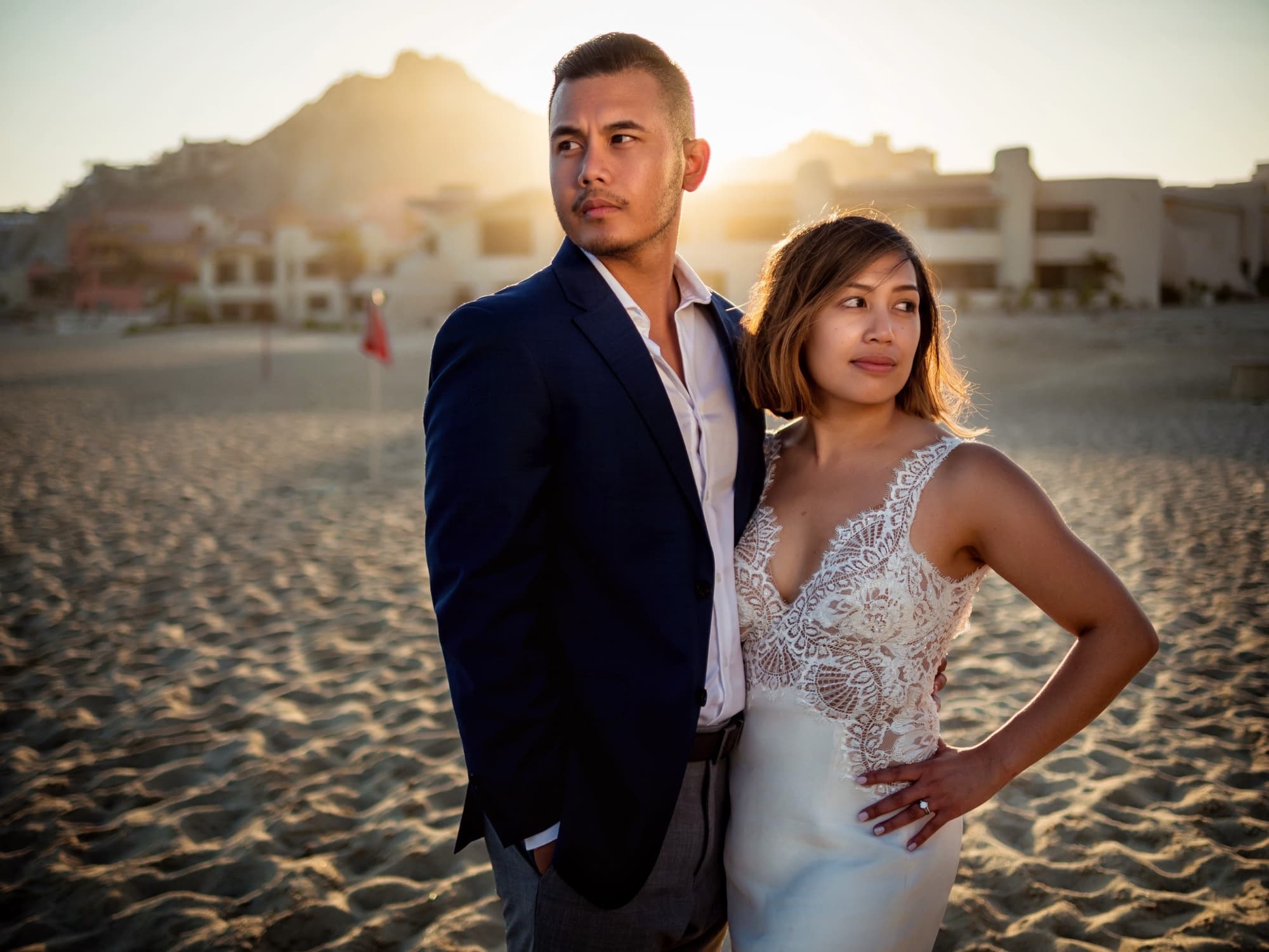 Editorial sunset portrait of Kirsten and Jolan on the Cabo beach with the desert mountains and sun flare behind them
