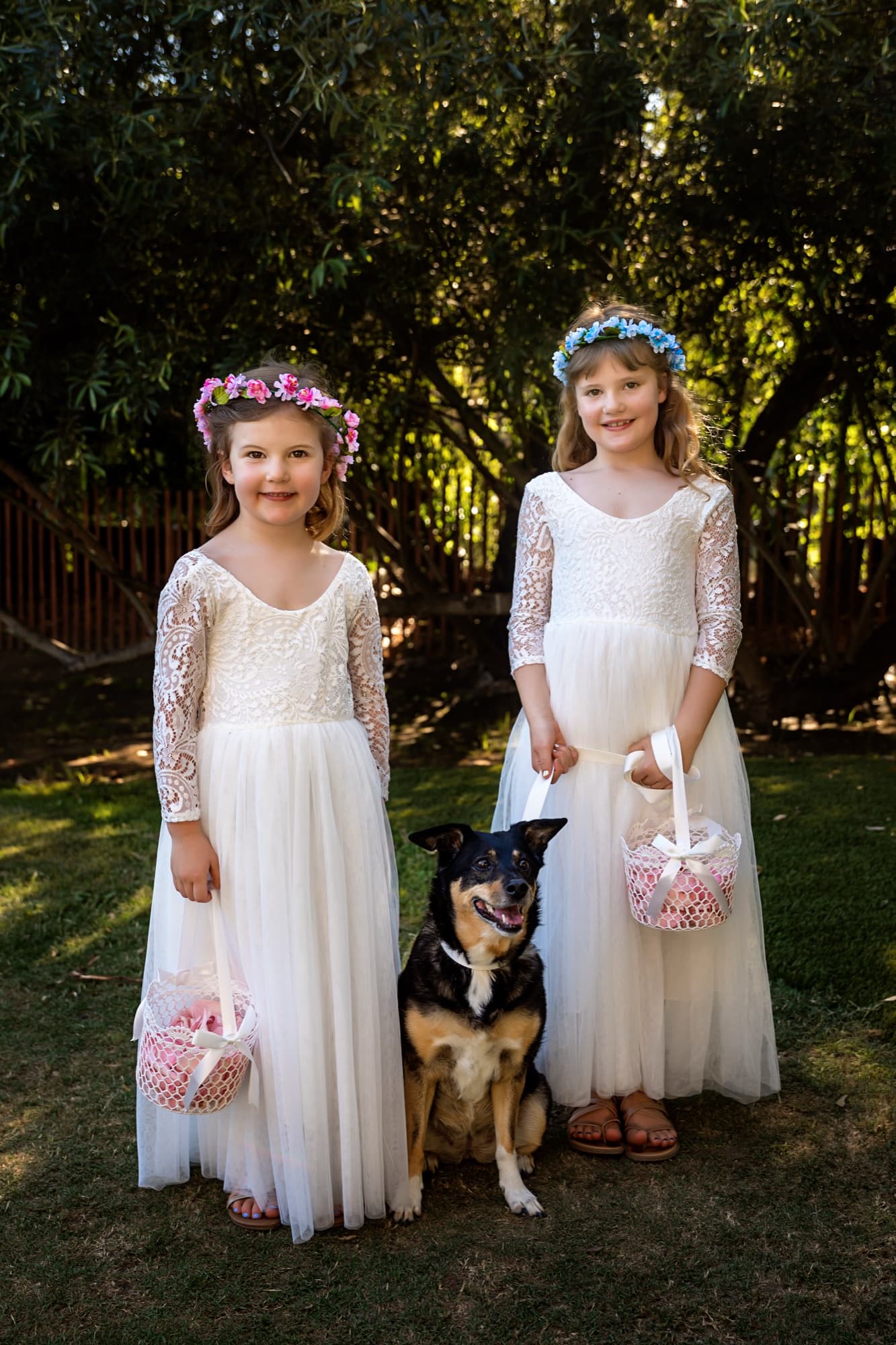 Two flower girls in white dresses and flower crowns standing with the family dog holding a flower basket at Calamigos Ranch