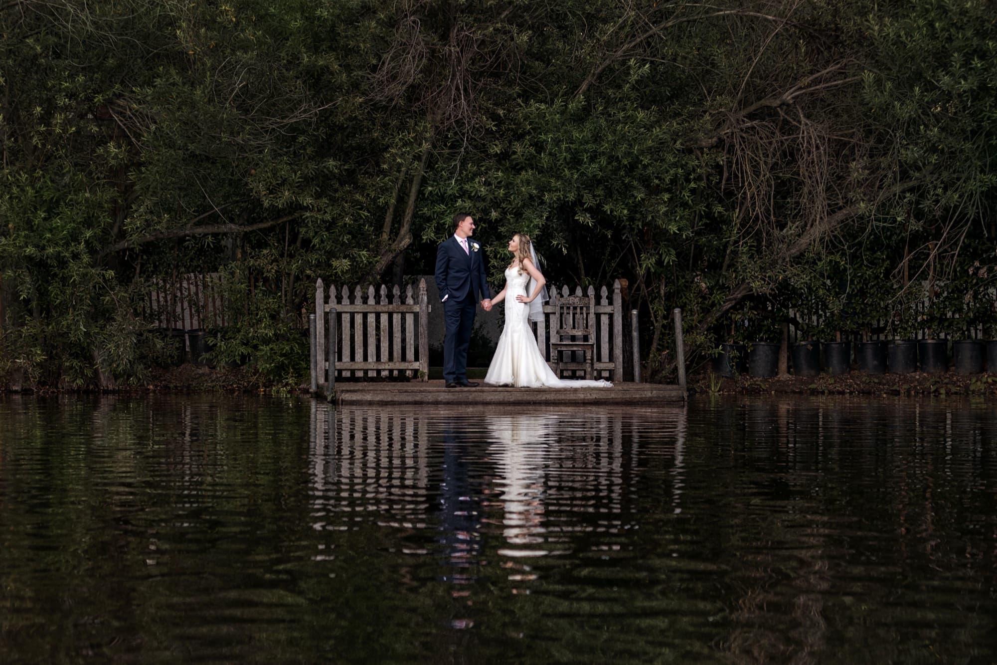 Monica and Colin standing on the wooden dock over the Calamigos Ranch lake, the water reflecting the trees around them