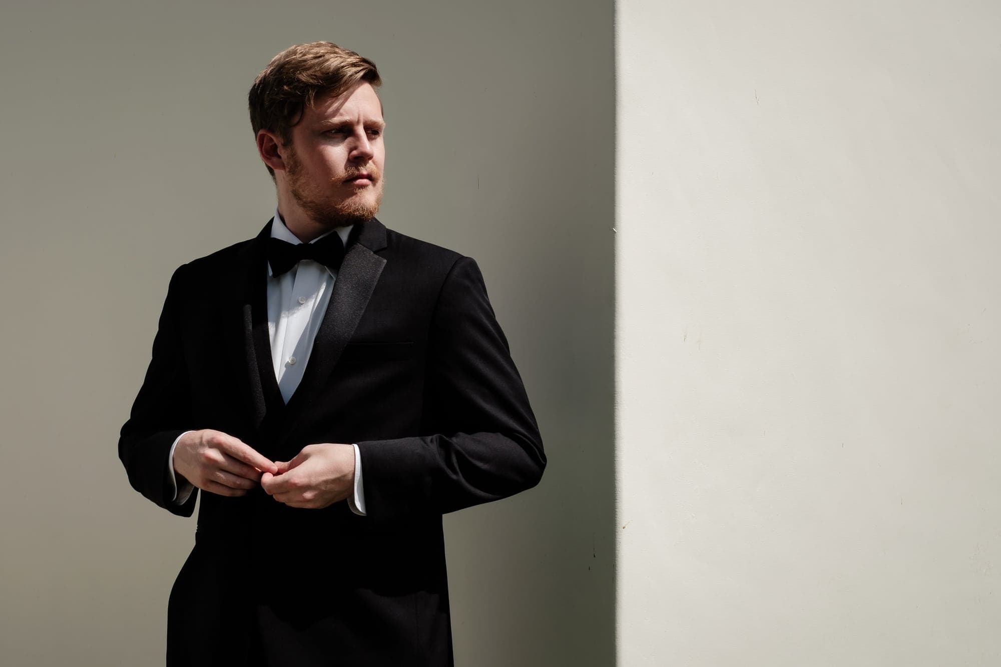 Alexander adjusting his black tuxedo in window light before the Calamigos Ranch ceremony