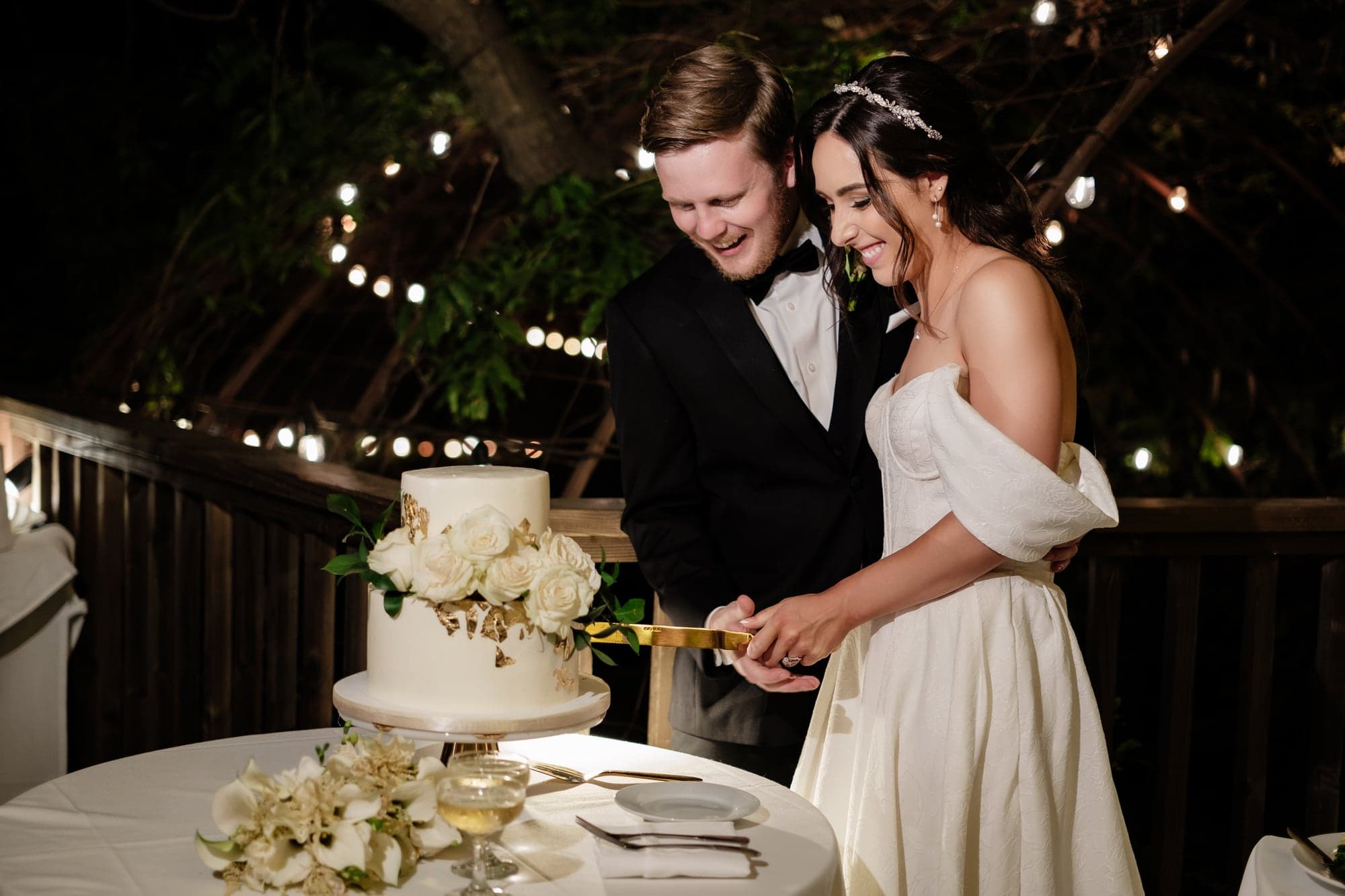 The couple cutting their wedding cake beneath string lights at Calamigos Ranch