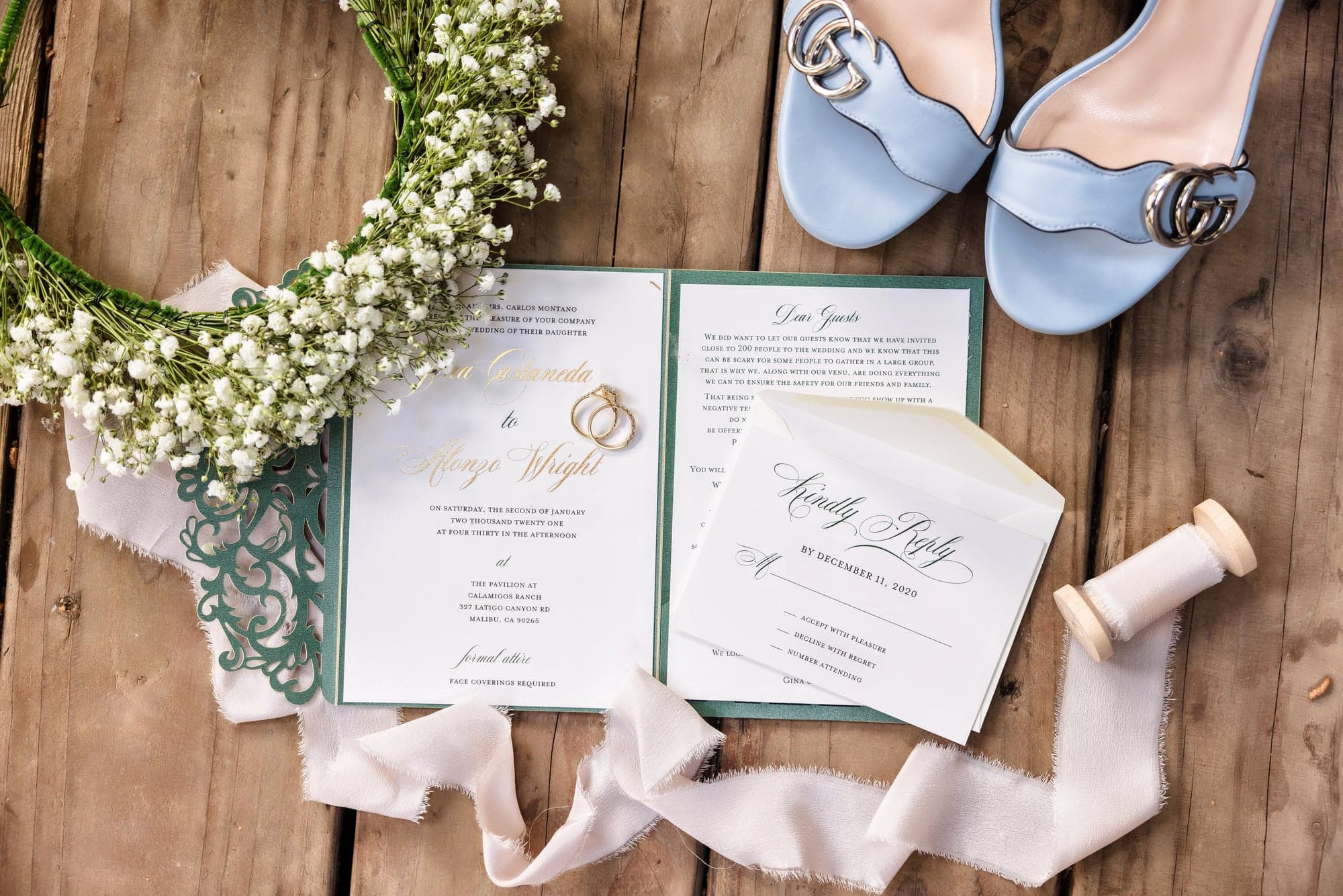 Blue wedding shoes, rings, stationery, and greenery arranged on wood for Gina and Alonso's wedding