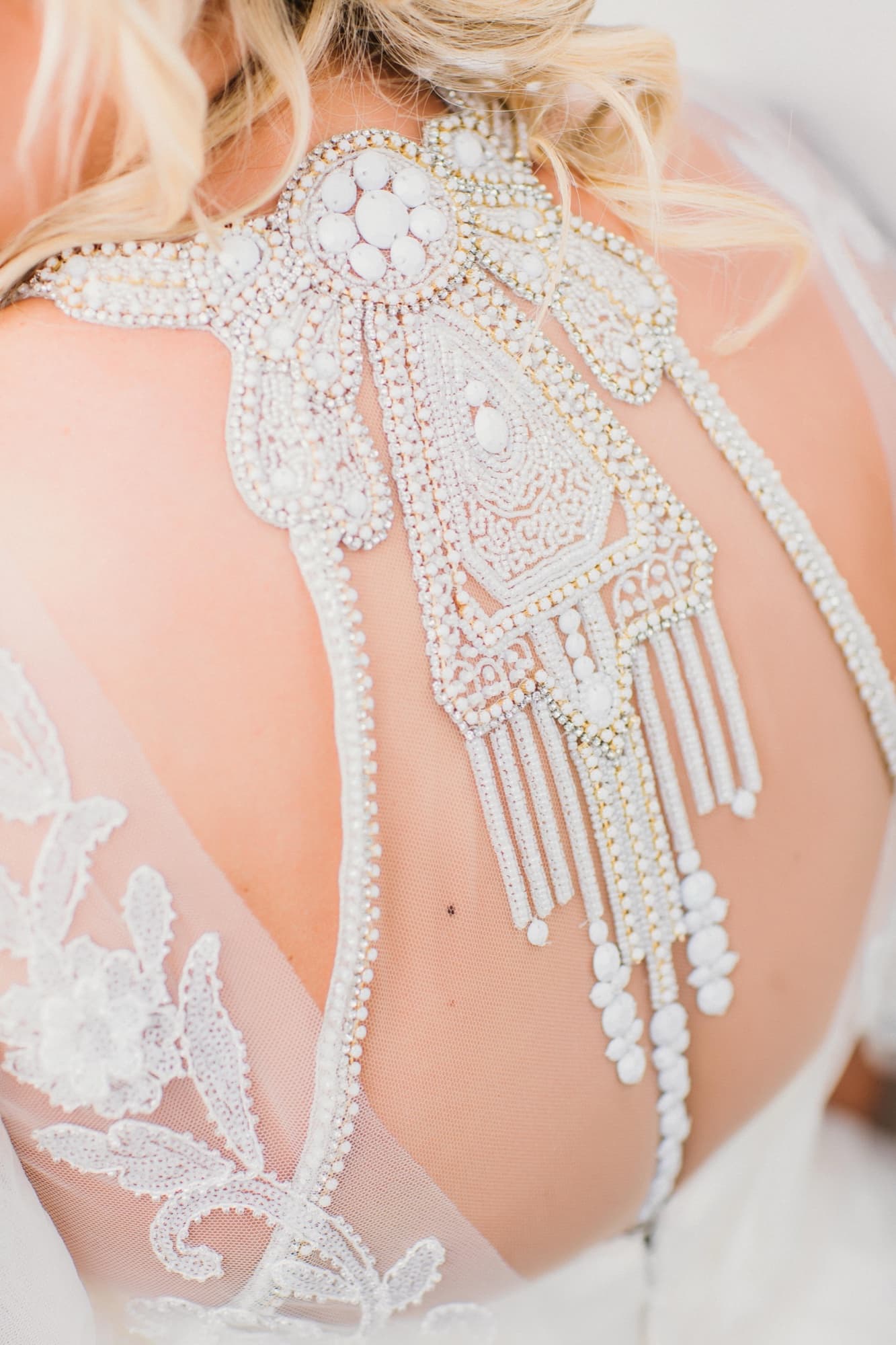 Close-up of the crystal-beaded back panel of the bride's gown draping across sheer lace