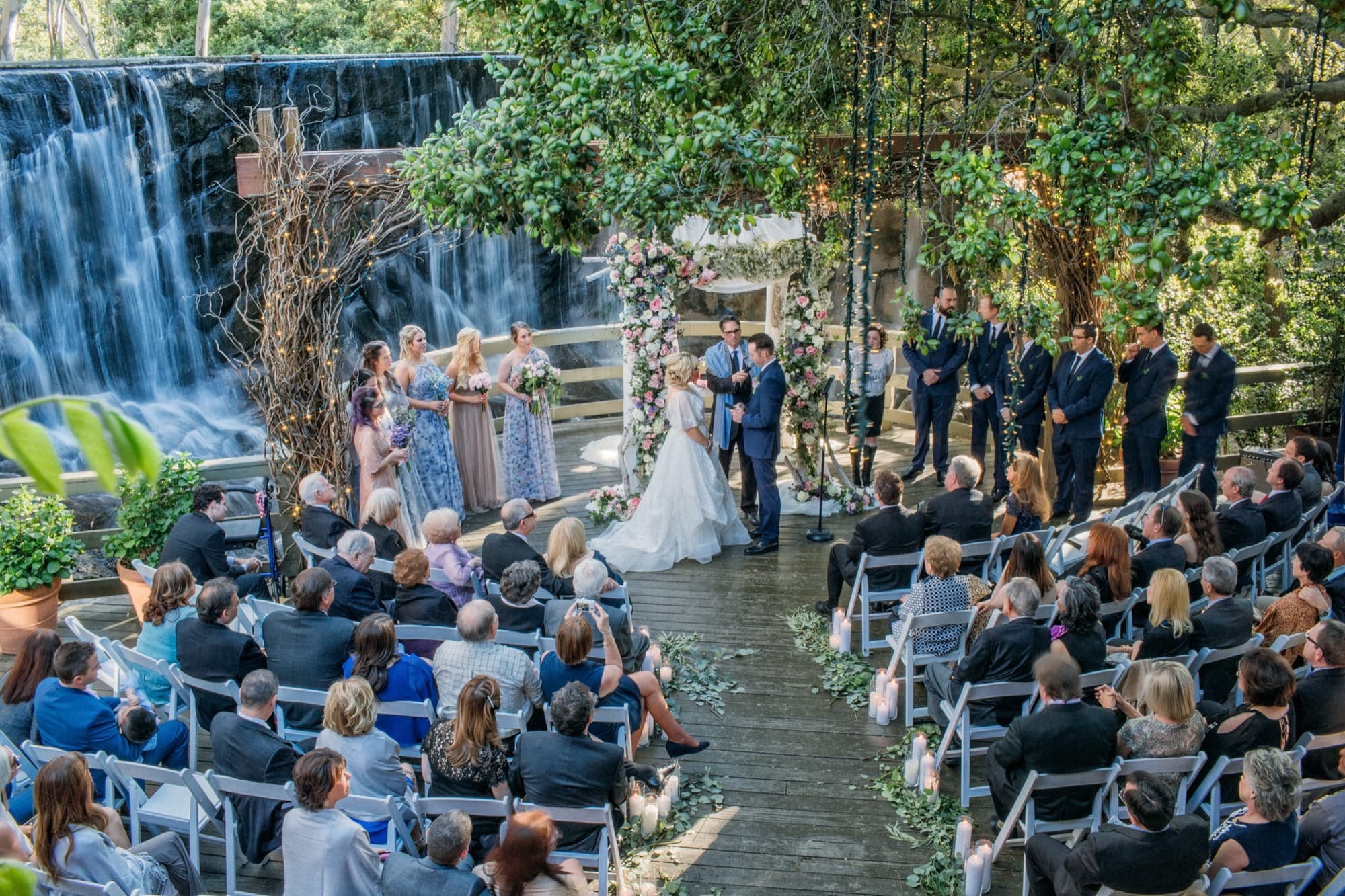 Wide view of the wedding ceremony at Calamigos Ranch with the waterfall cascading behind the wedding party and guests