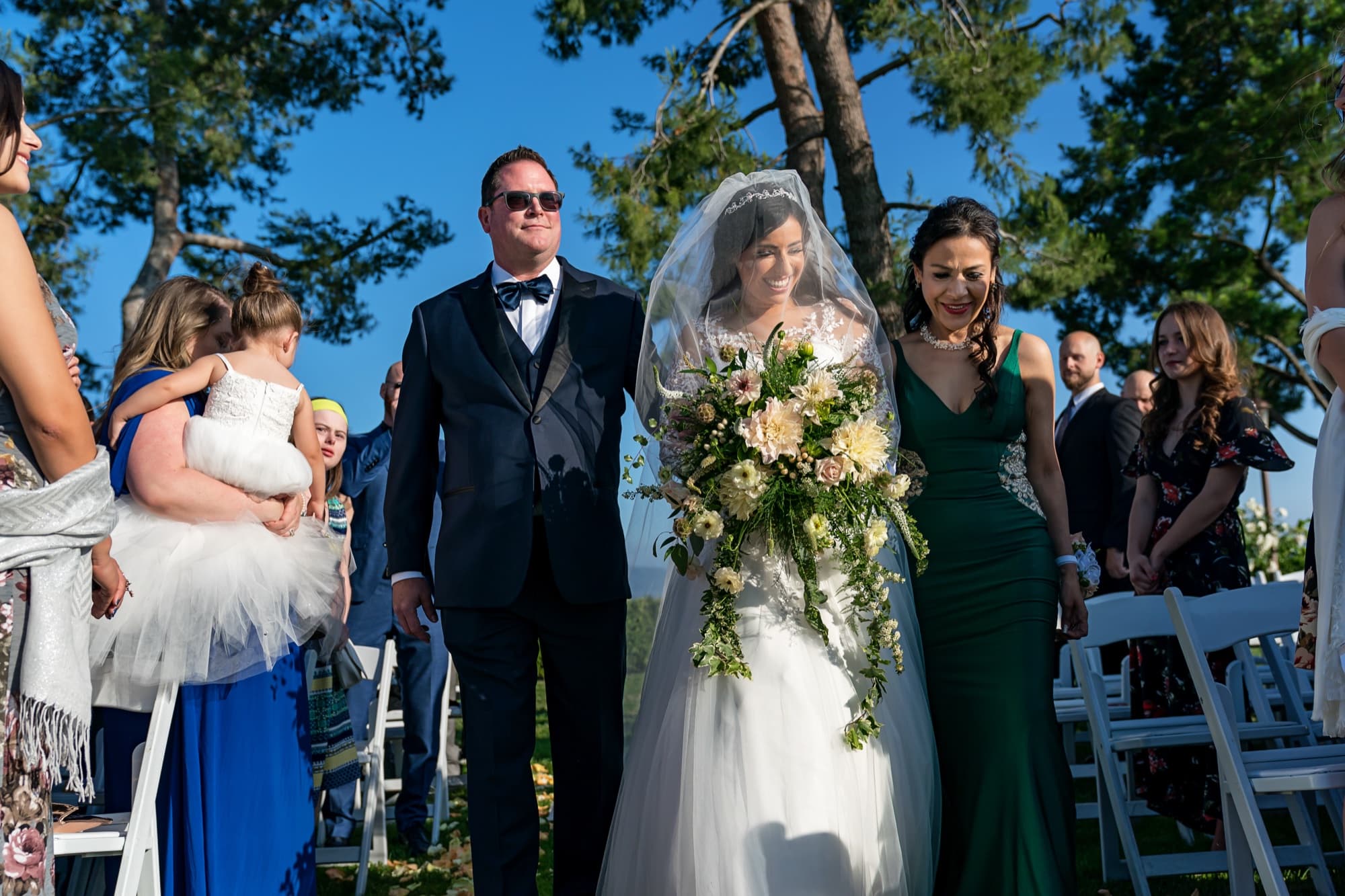 Tania walking down the outdoor aisle on her father's arm with a lush bouquet at Callaway Vineyard in Temecula