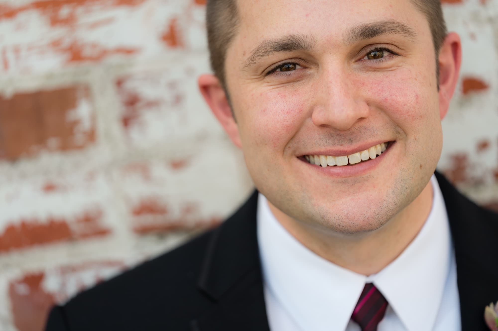 Peter smiling in a black suit and burgundy tie against the whitewashed brick of Carondelet House