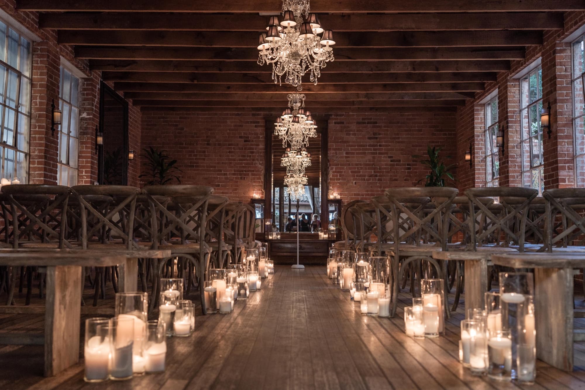 The candlelit ceremony aisle at Carondelet House lined with hundreds of pillar candles beneath two crystal chandeliers