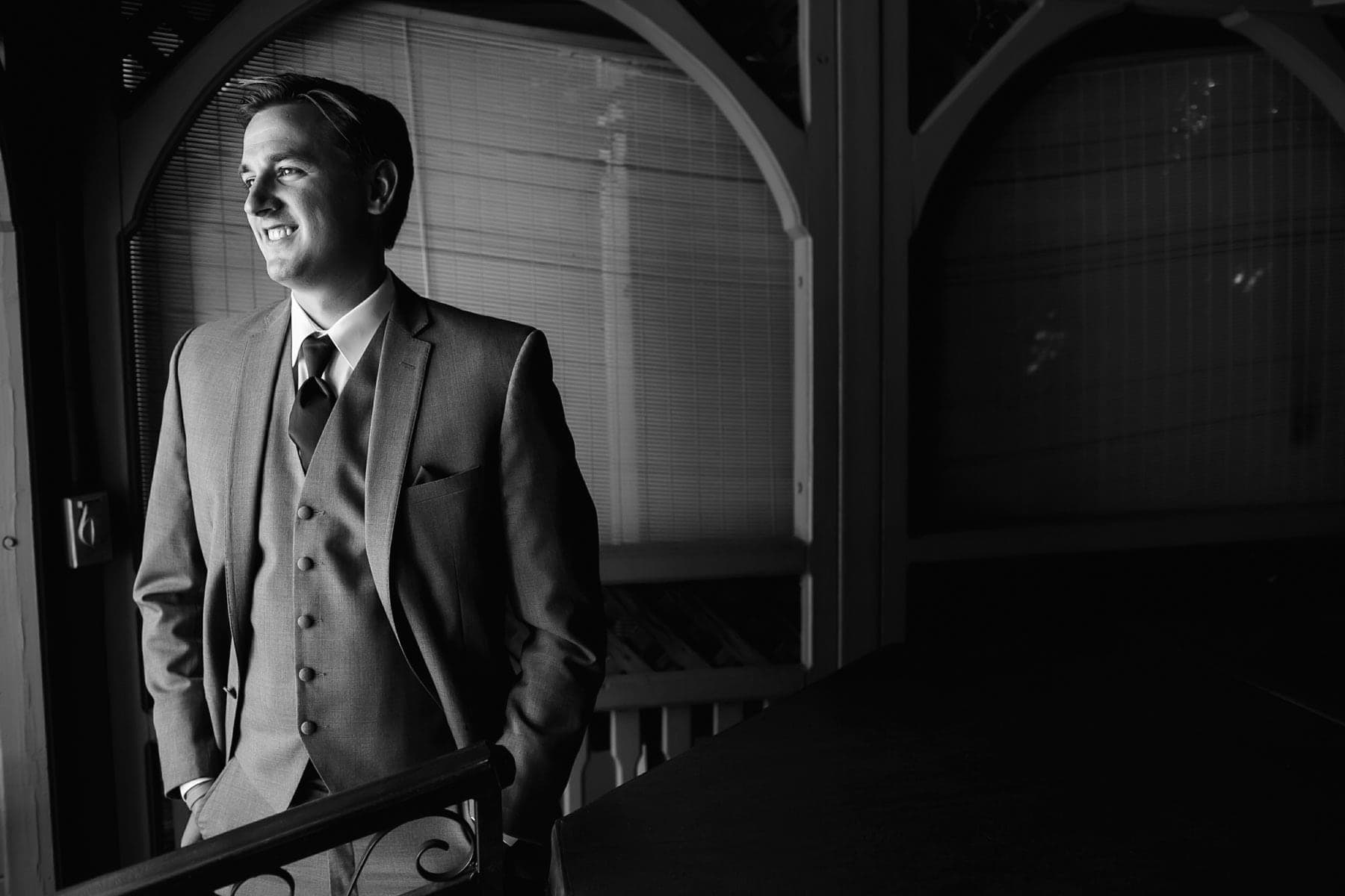 Groom standing beside an arched window