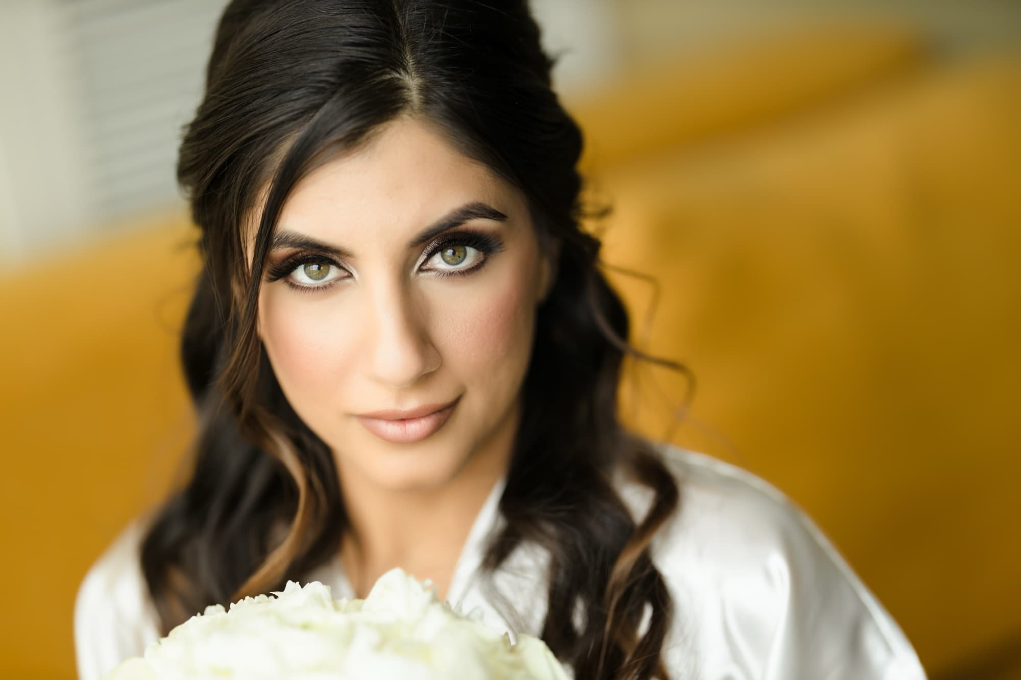 Beauty portrait of Hela with soft waves and glowing makeup behind her bouquet of white roses