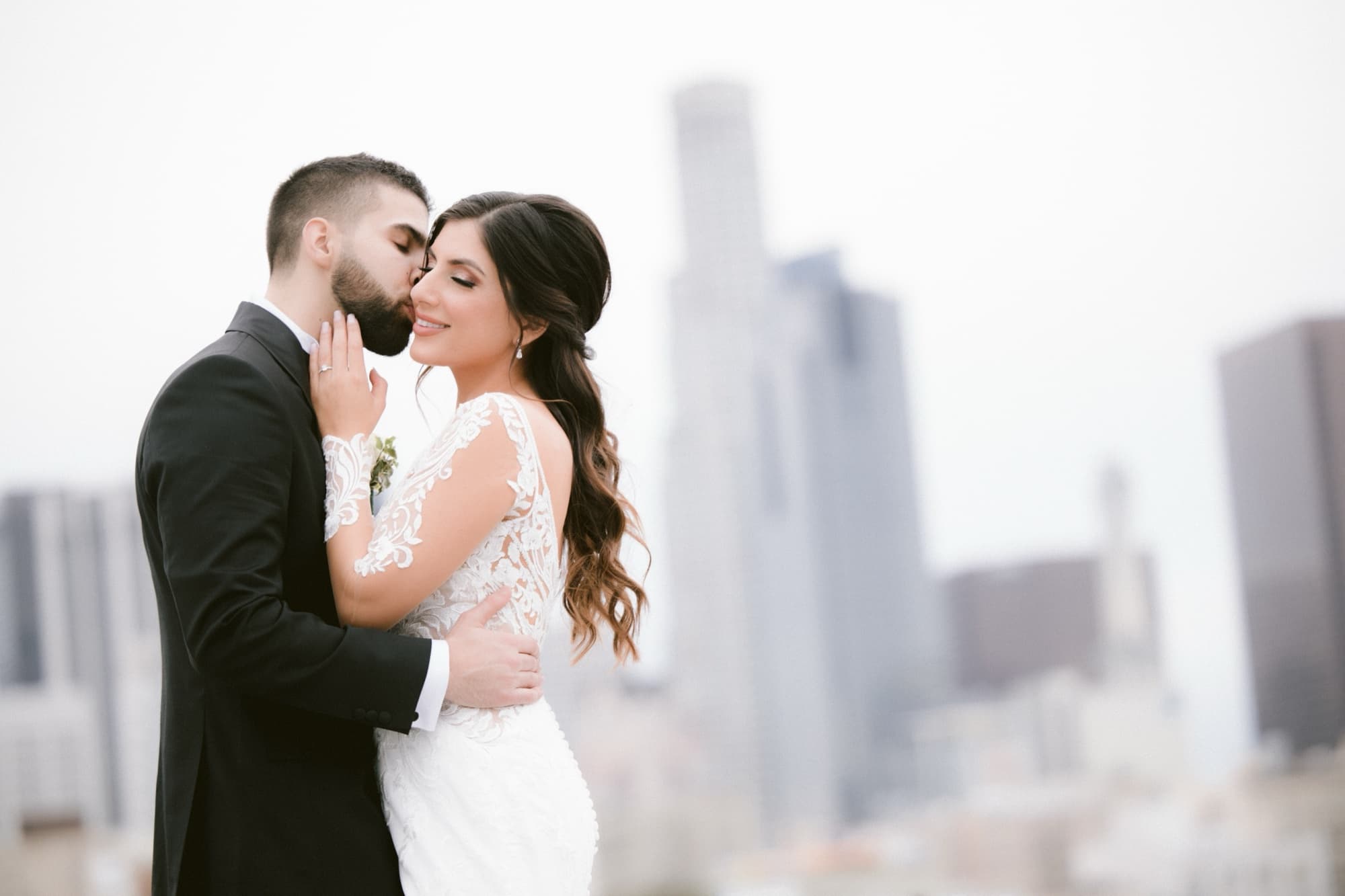 Hela and Yousef kissing on the rooftop as the downtown Los Angeles towers soften into the haze behind them