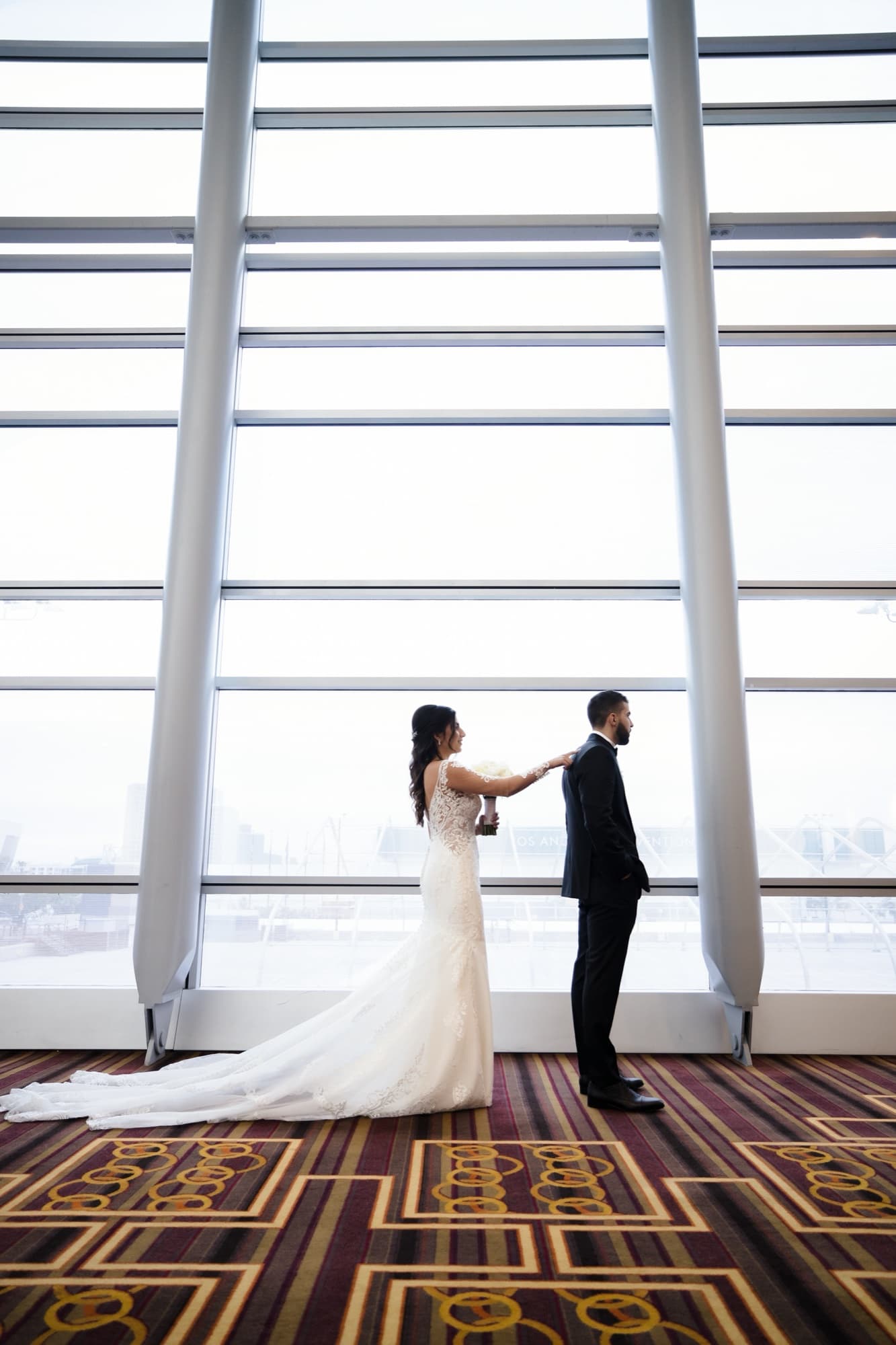 Hela and Yousef holding hands at City Club LA's floor-to-ceiling windows, downtown Los Angeles stretched out below
