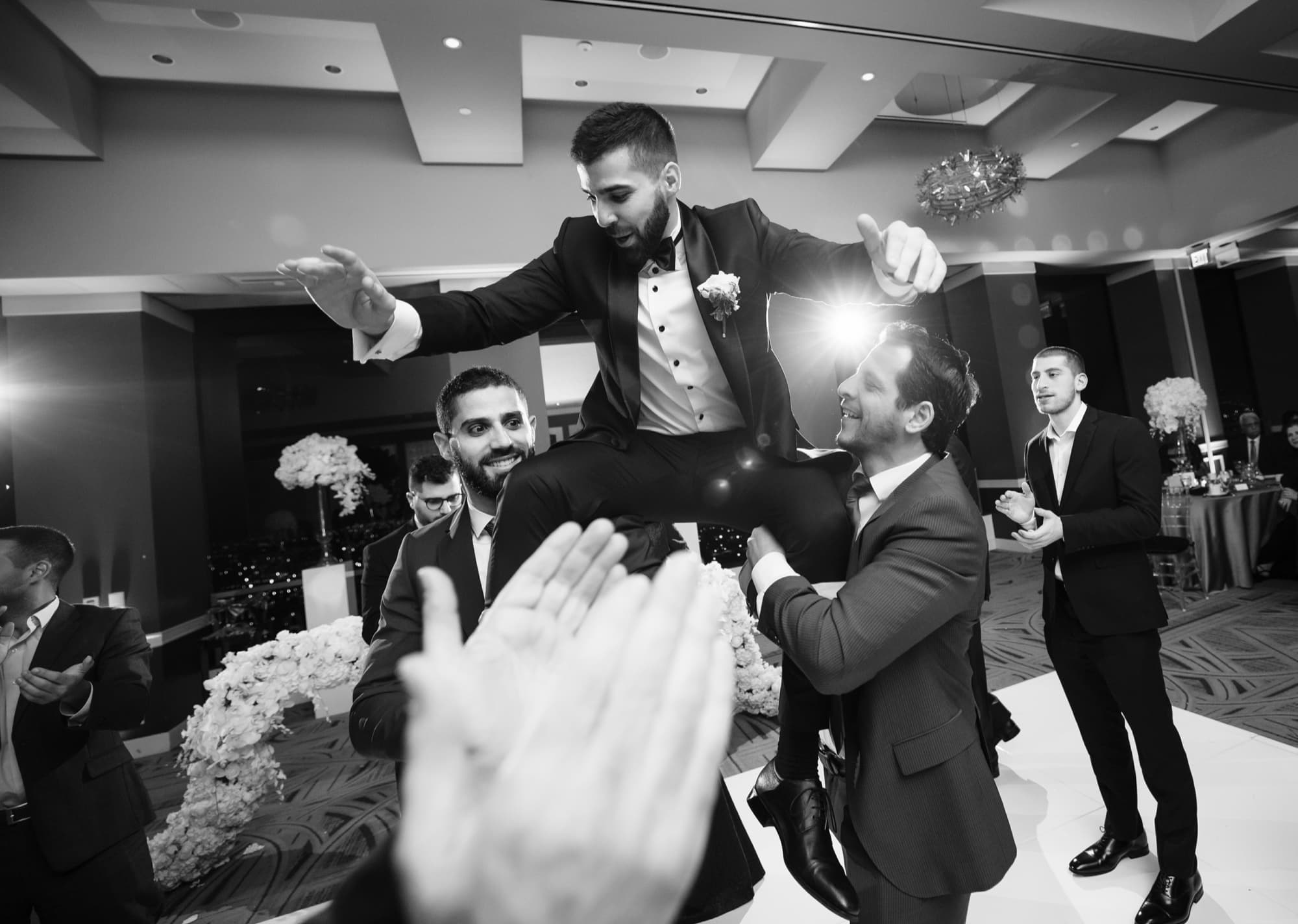 Black and white photograph of Yousef hoisted on shoulders above the dance floor as guests celebrate around him