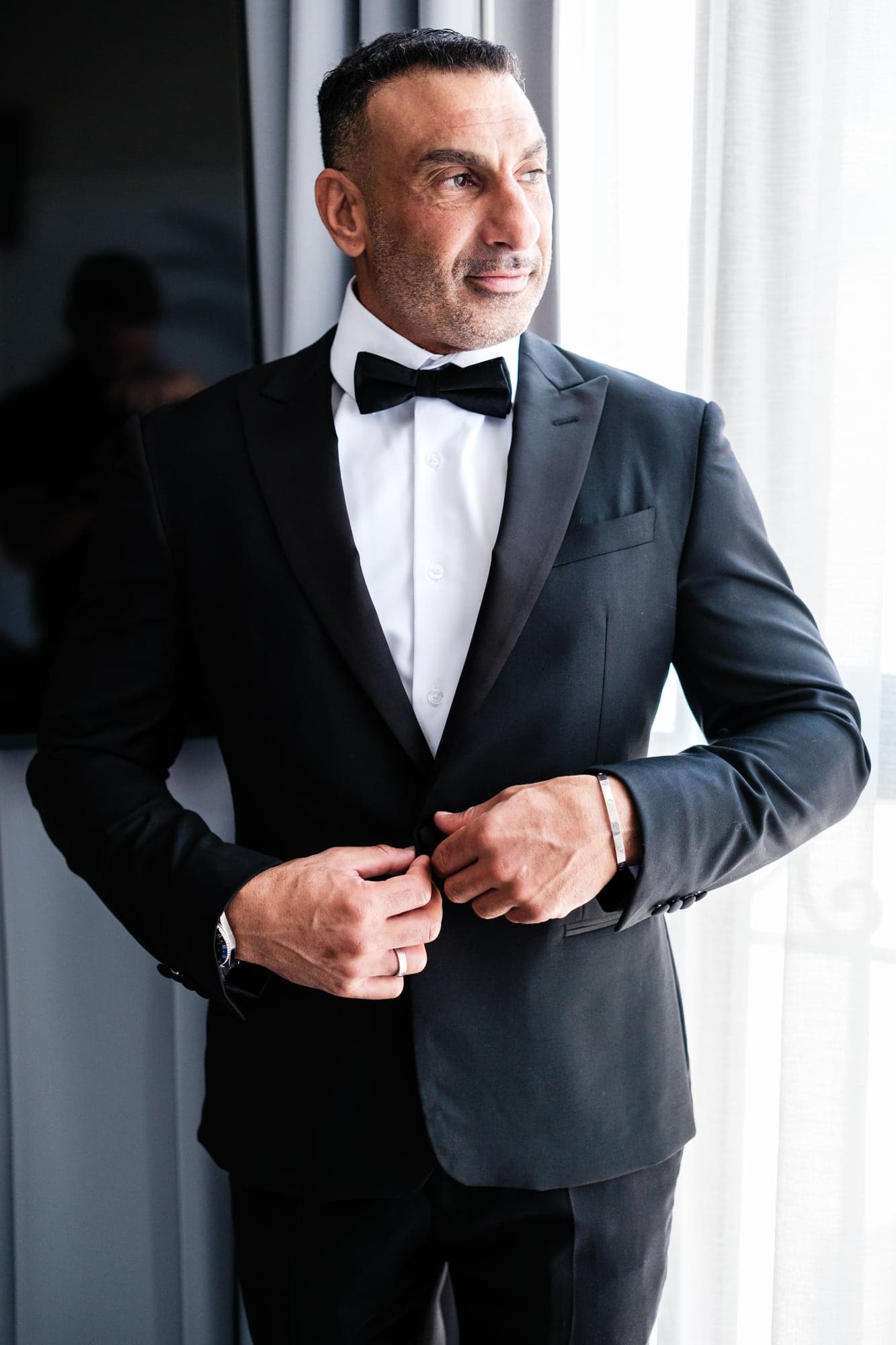 Sherif standing in window light in his tuxedo before the Coptic ceremony