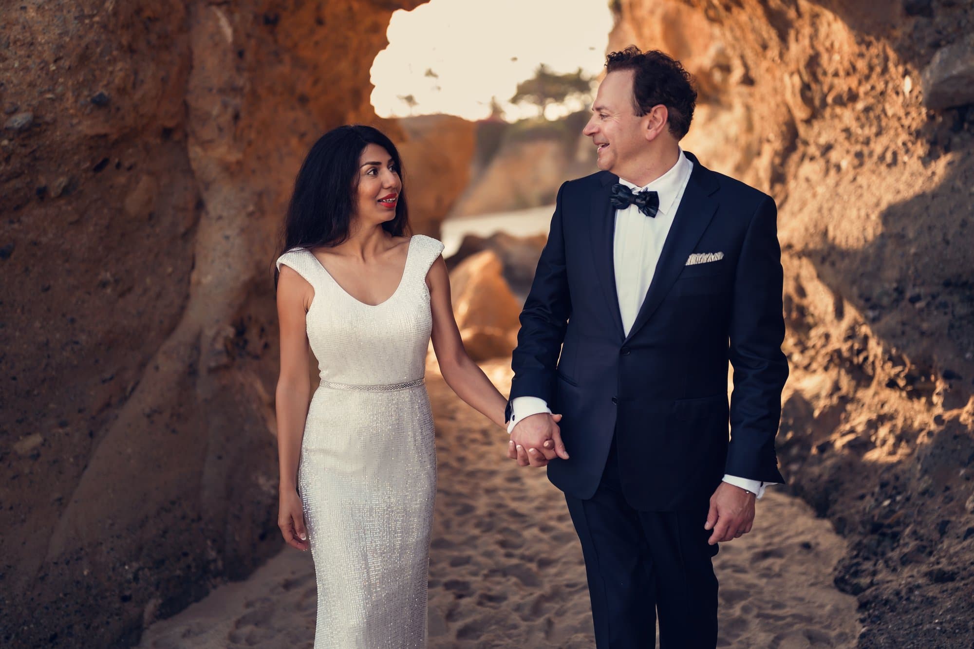 A couple walking hand in hand through a golden sea cave at Laguna Beach
