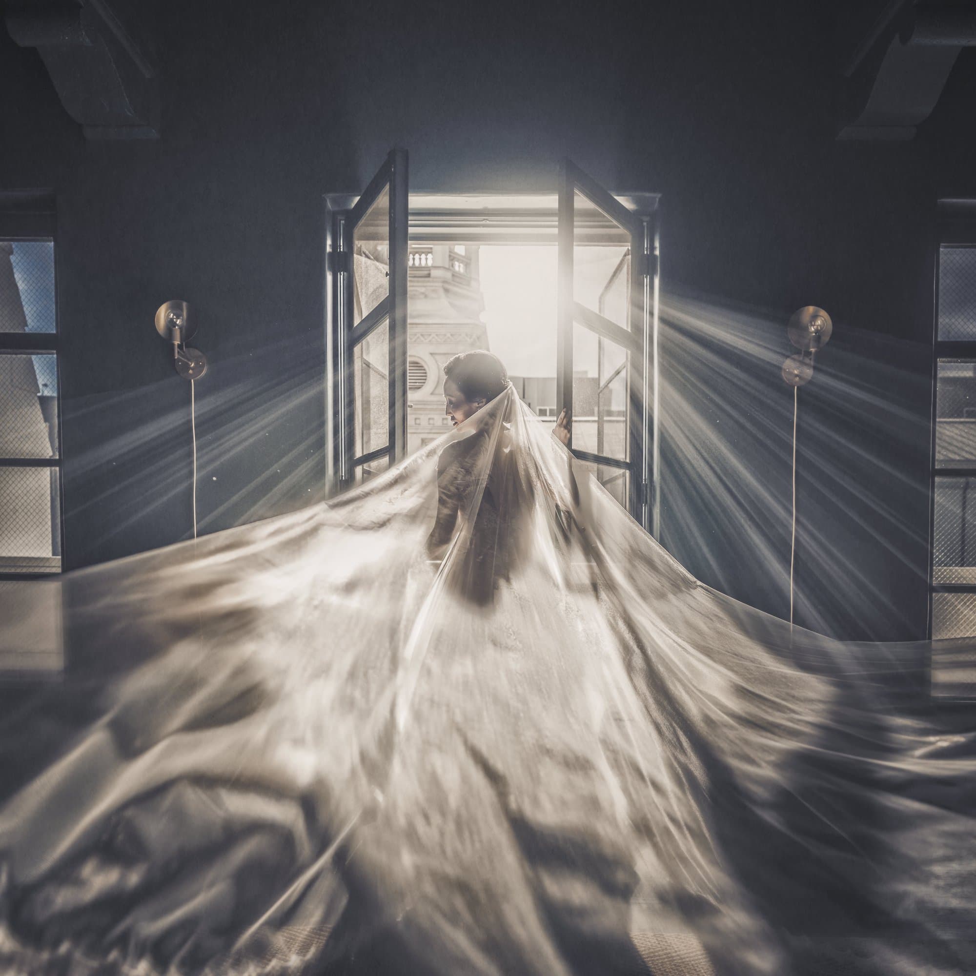 A bride's cathedral veil sweeping through open doors as beams of light pour into a dark hall