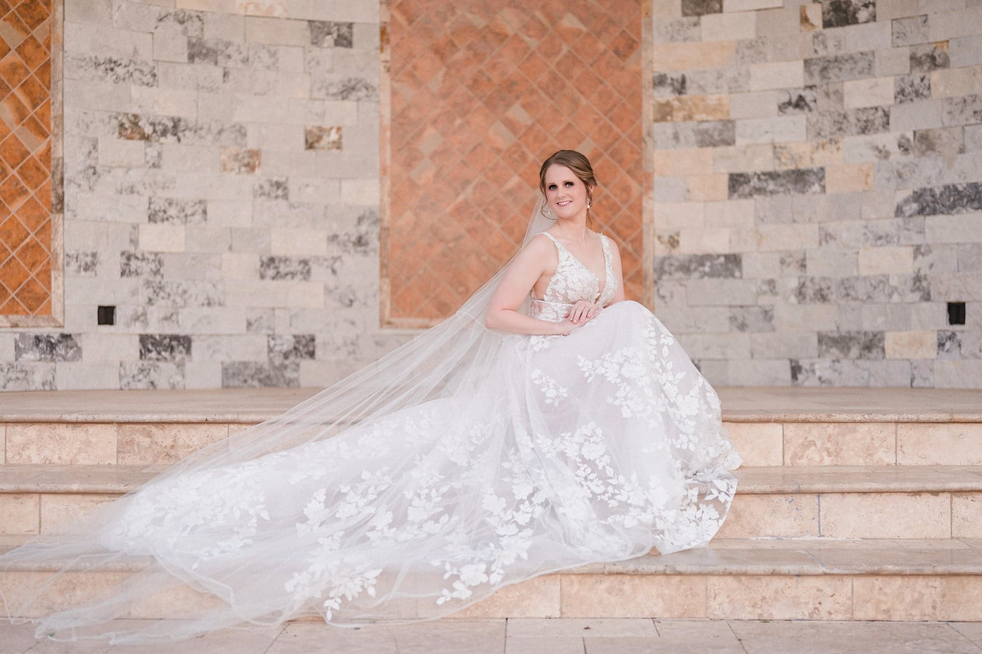 Erin seated on the travertine steps at D'Vine Grace Vineyard with her floral lace gown and cathedral veil fanned out beside her