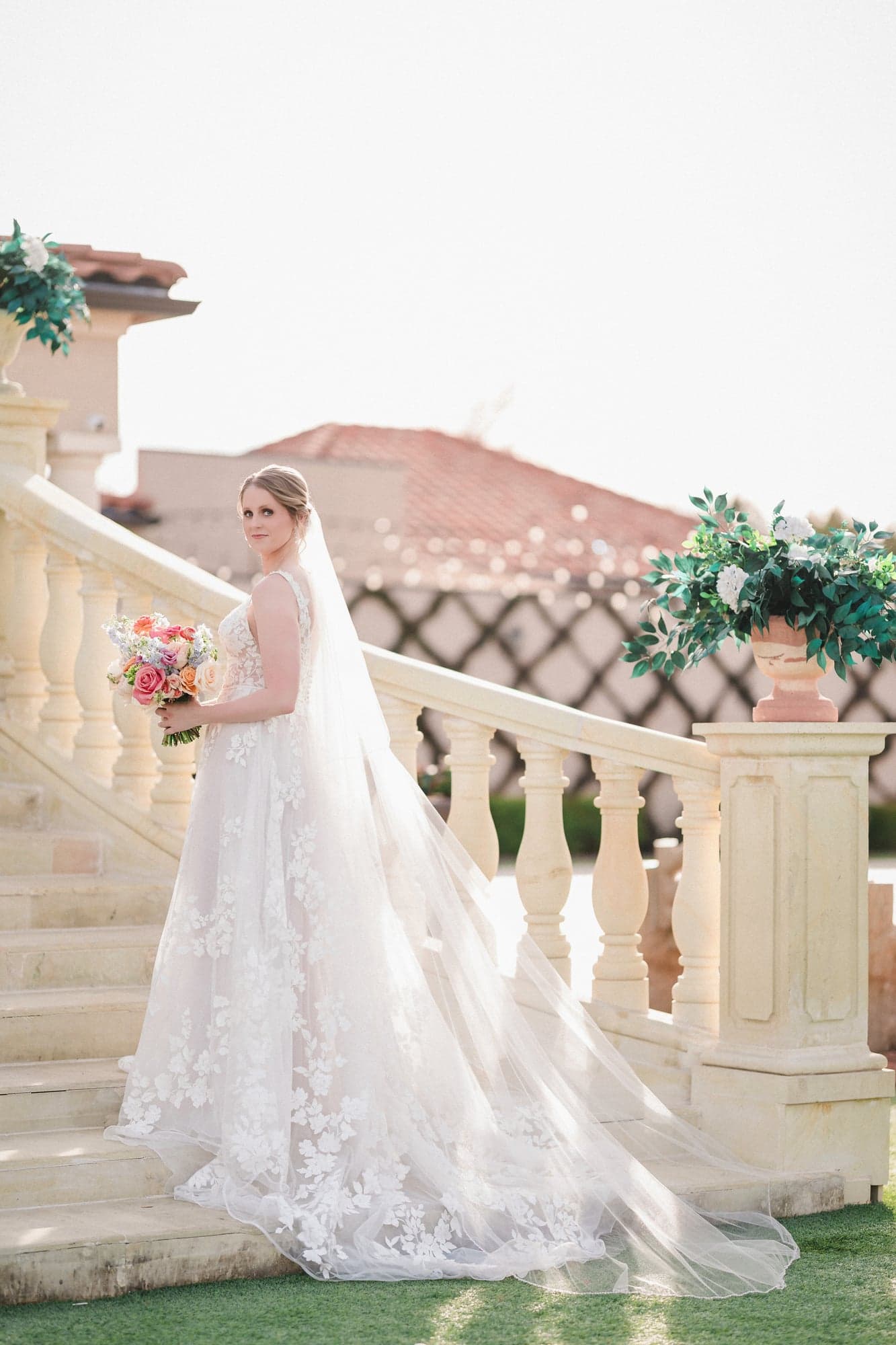 Erin on the estate's curved stone staircase in her lace gown, veil trailing down the steps behind her