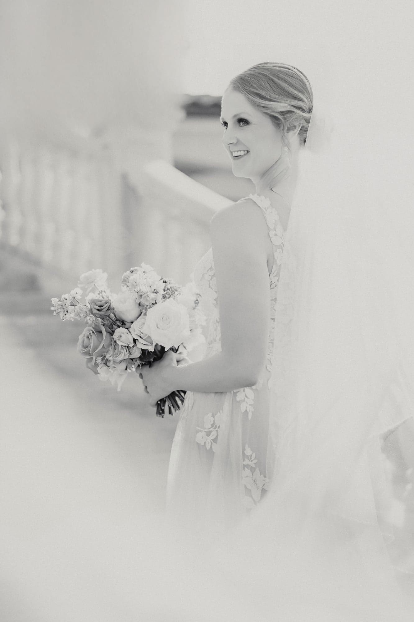 High-key black and white bridal portrait of Erin holding her bouquet with her veil across her shoulders