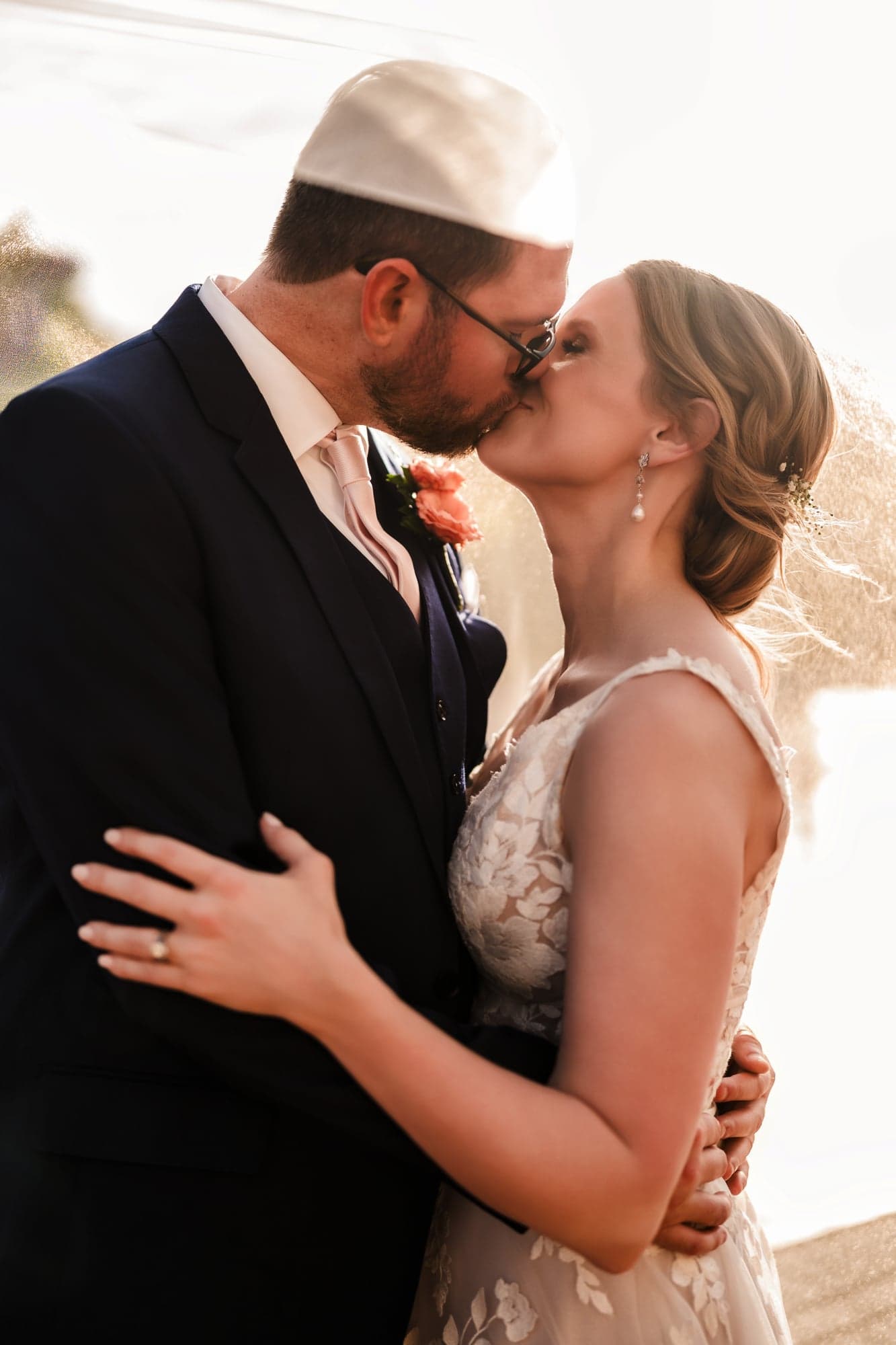 Erin and Hunter kissing in low evening sun with her veil lifting behind them