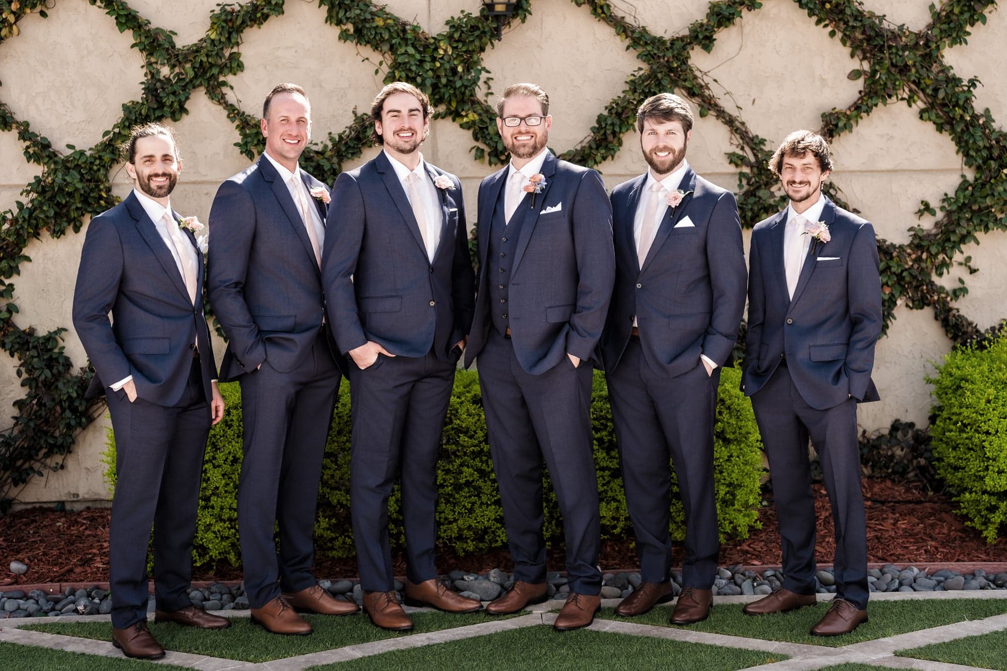 Hunter and his five groomsmen in navy suits standing against a lattice hedge