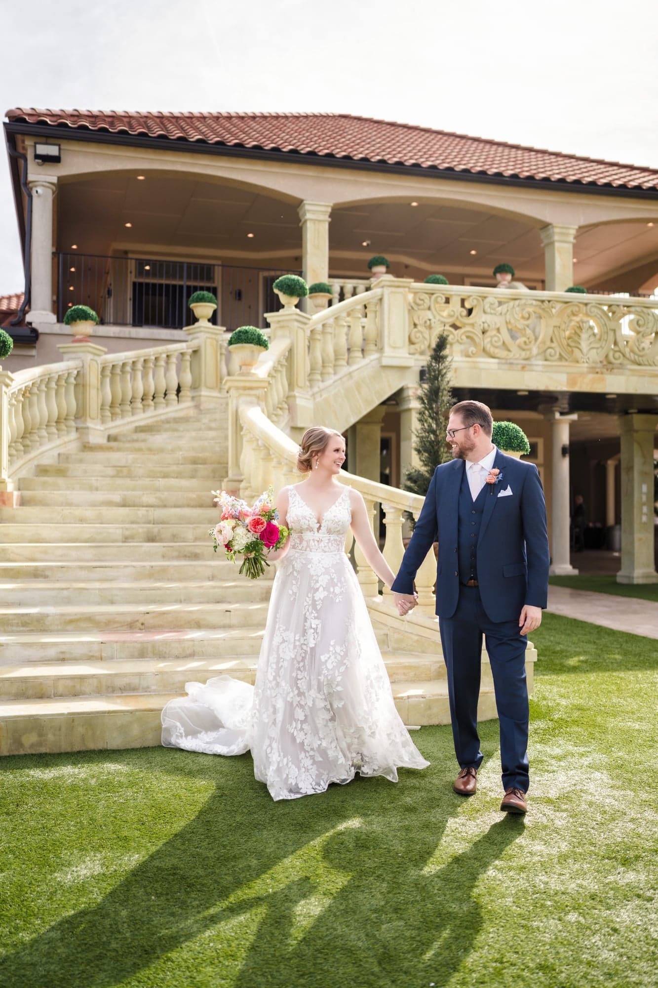 Erin and Hunter walking hand in hand across the lawn below the estate's twin staircases