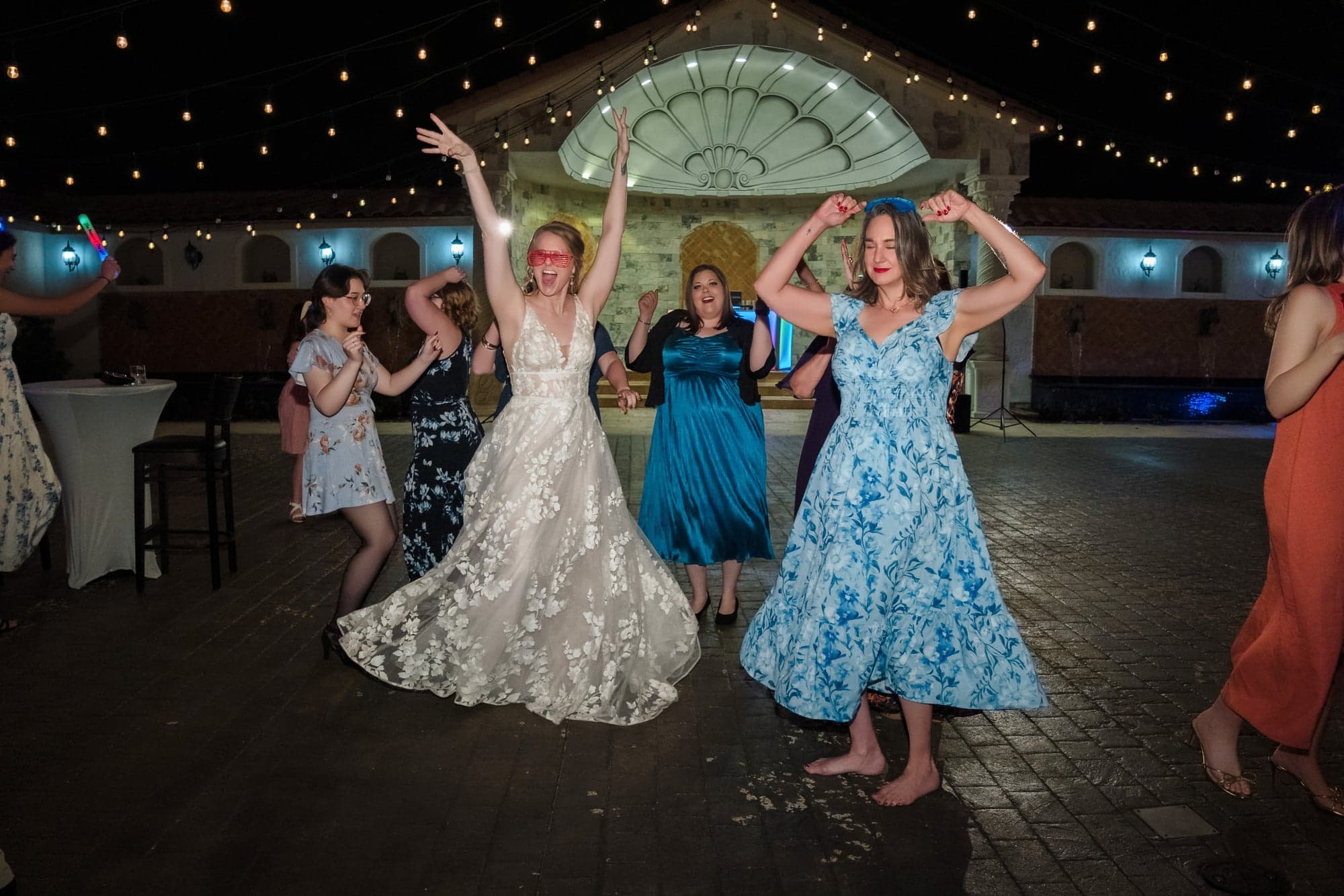 Erin dancing with her arms up on the string-lit outdoor terrace at night while guests dance around her