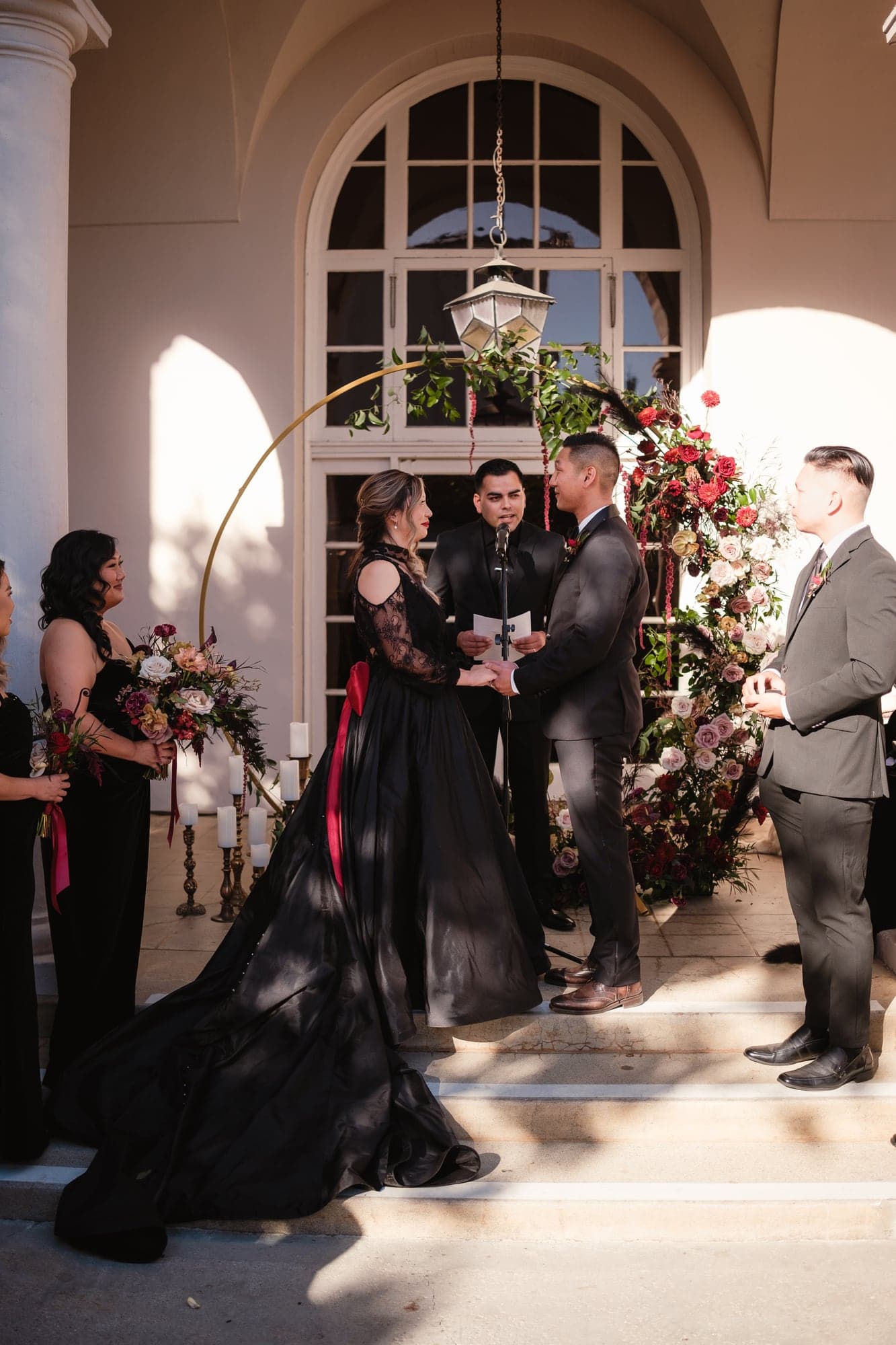 Alda and Kevin exchanging vows beneath the courtyard floral arch