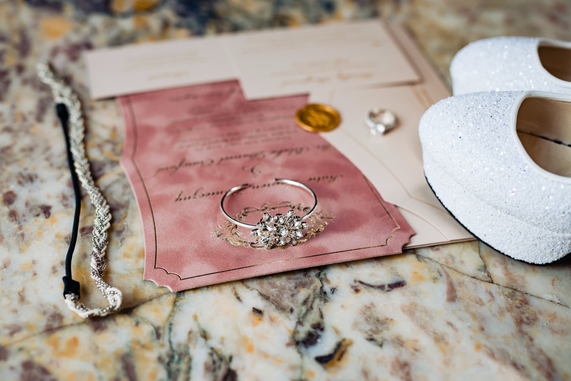 Blush suede invitation suite with wax seal, crystal bracelet, braided headpiece, and glitter platform heels on marble at the Ebell of Los Angeles