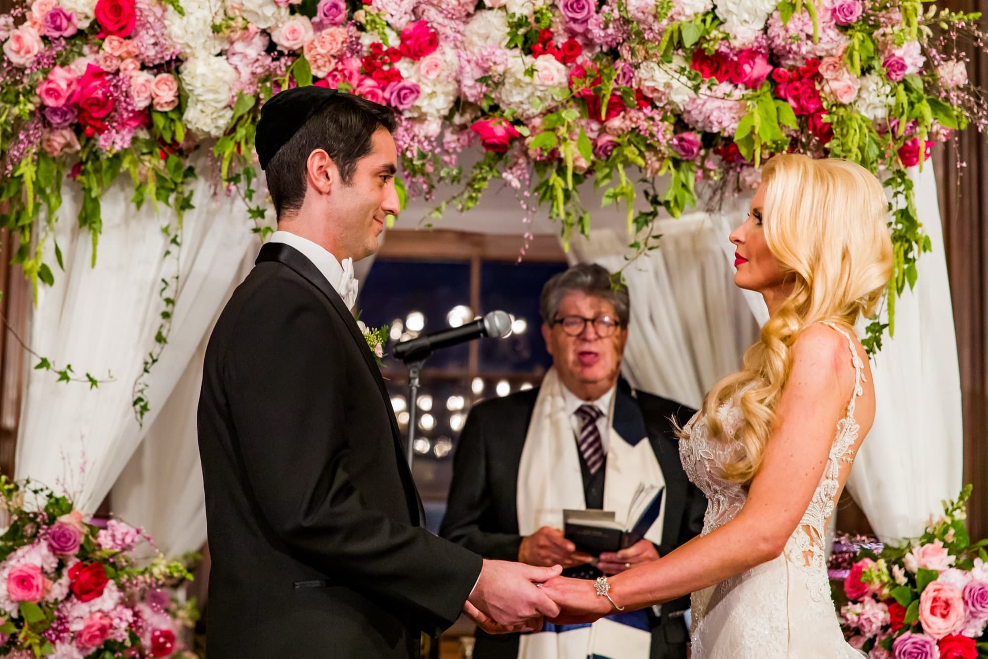 Katie and Blake holding hands beneath the rose-covered chuppah during their vows at the Ebell of Los Angeles