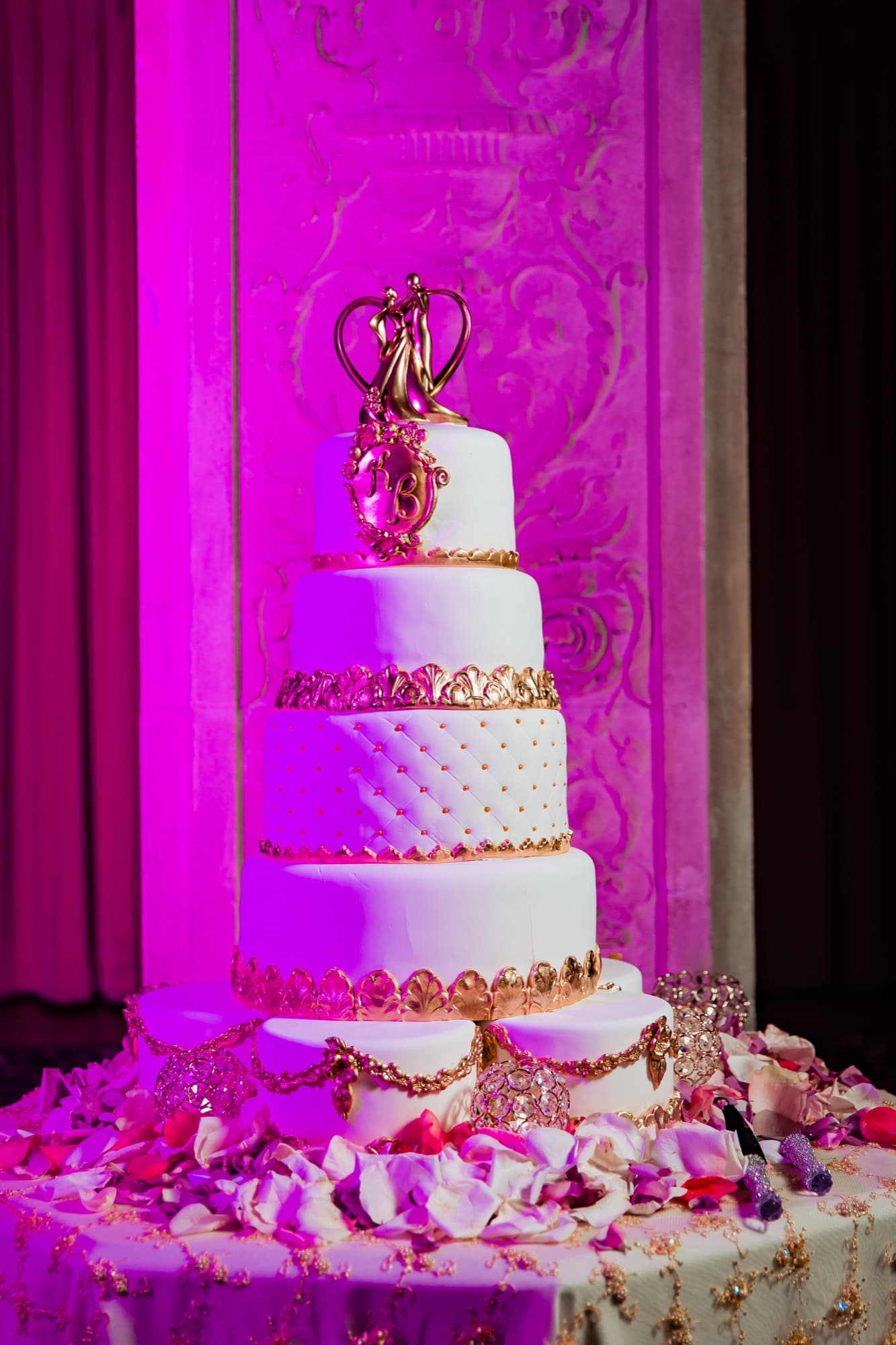 Gold-detailed white wedding cake with a sculptural topper washed in magenta uplight at the Ebell reception