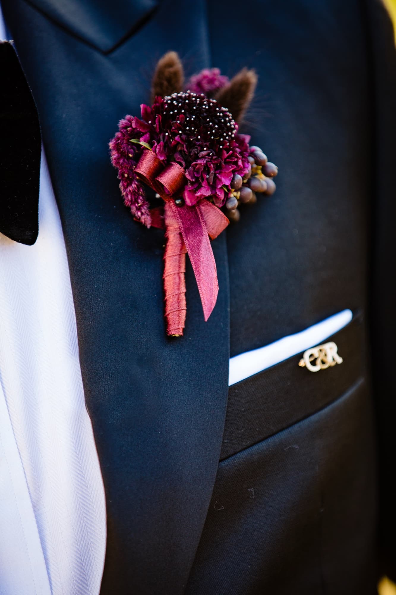 Christopher's burgundy boutonniere and gold C and R monogram pin on his black tuxedo lapel