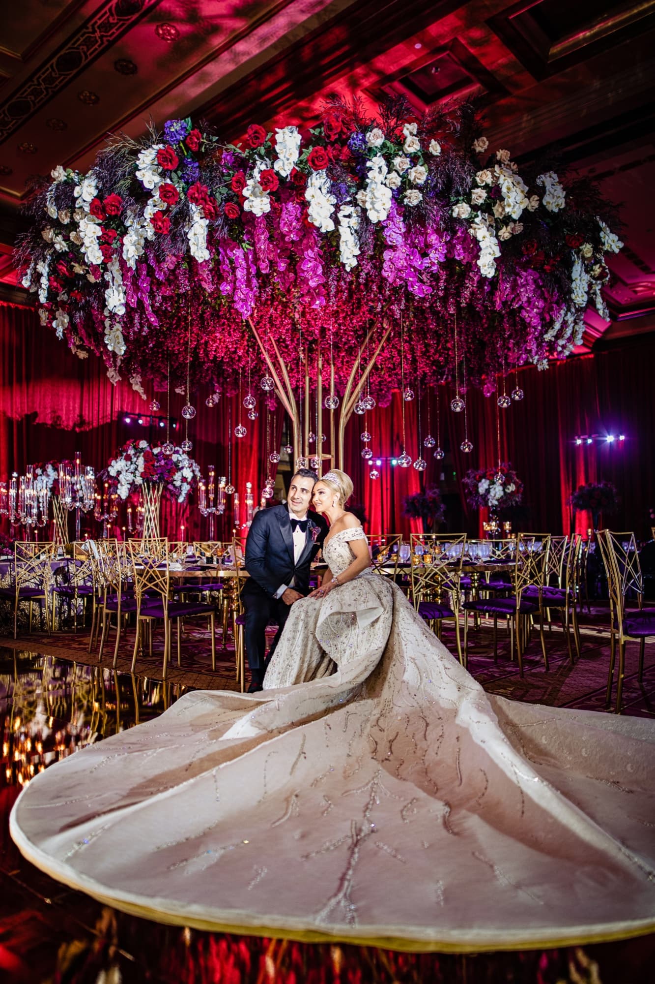 Rhonda and Christopher in the Fairmont Grand Del Mar ballroom beneath hanging florals, her beaded train fanned in a full circle