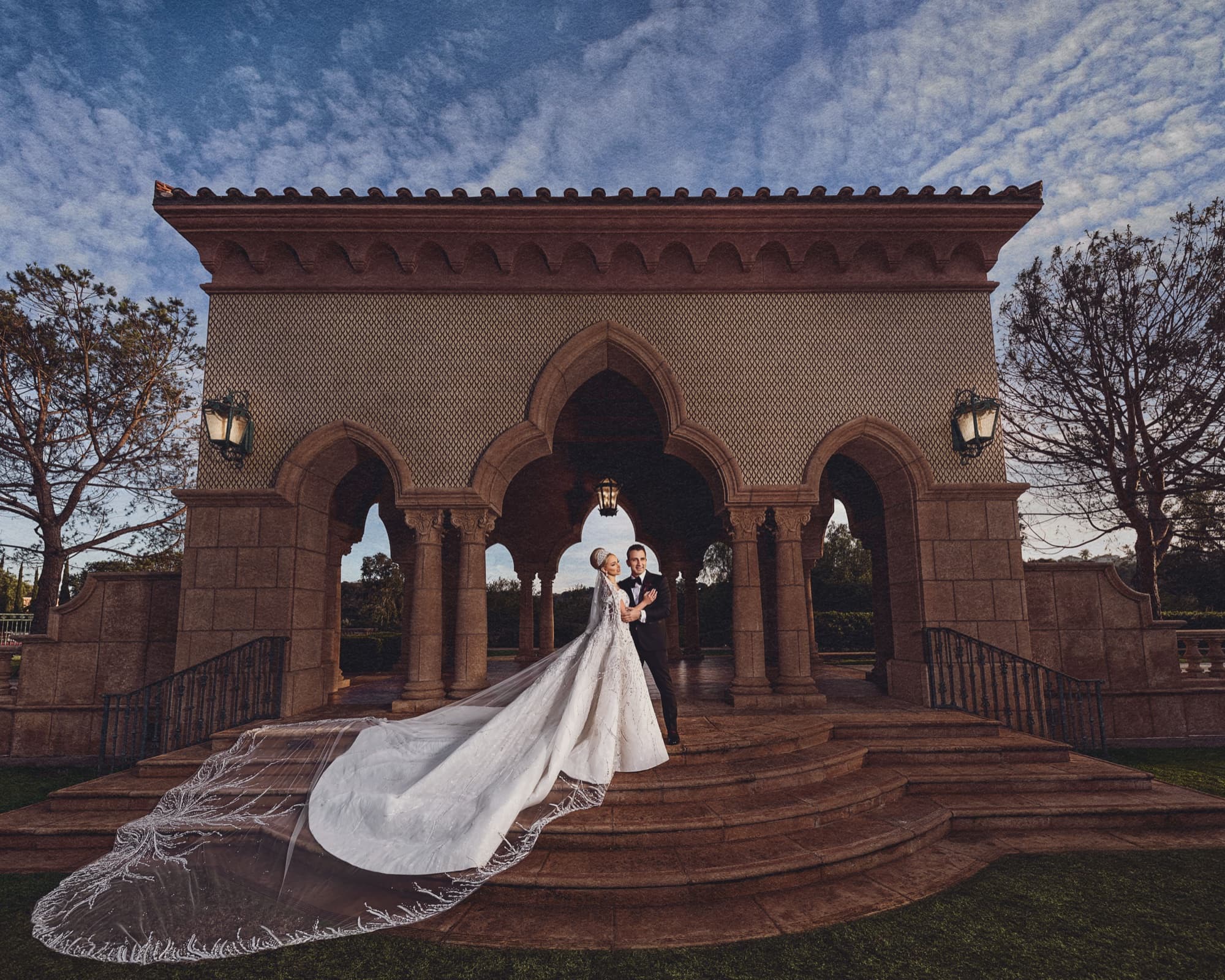 Rhonda and Christopher standing beneath the Moorish arches of the Fairmont Grand Del Mar at dusk, her cathedral train cascading down the stone steps, photographed by Michael Anthony Photography