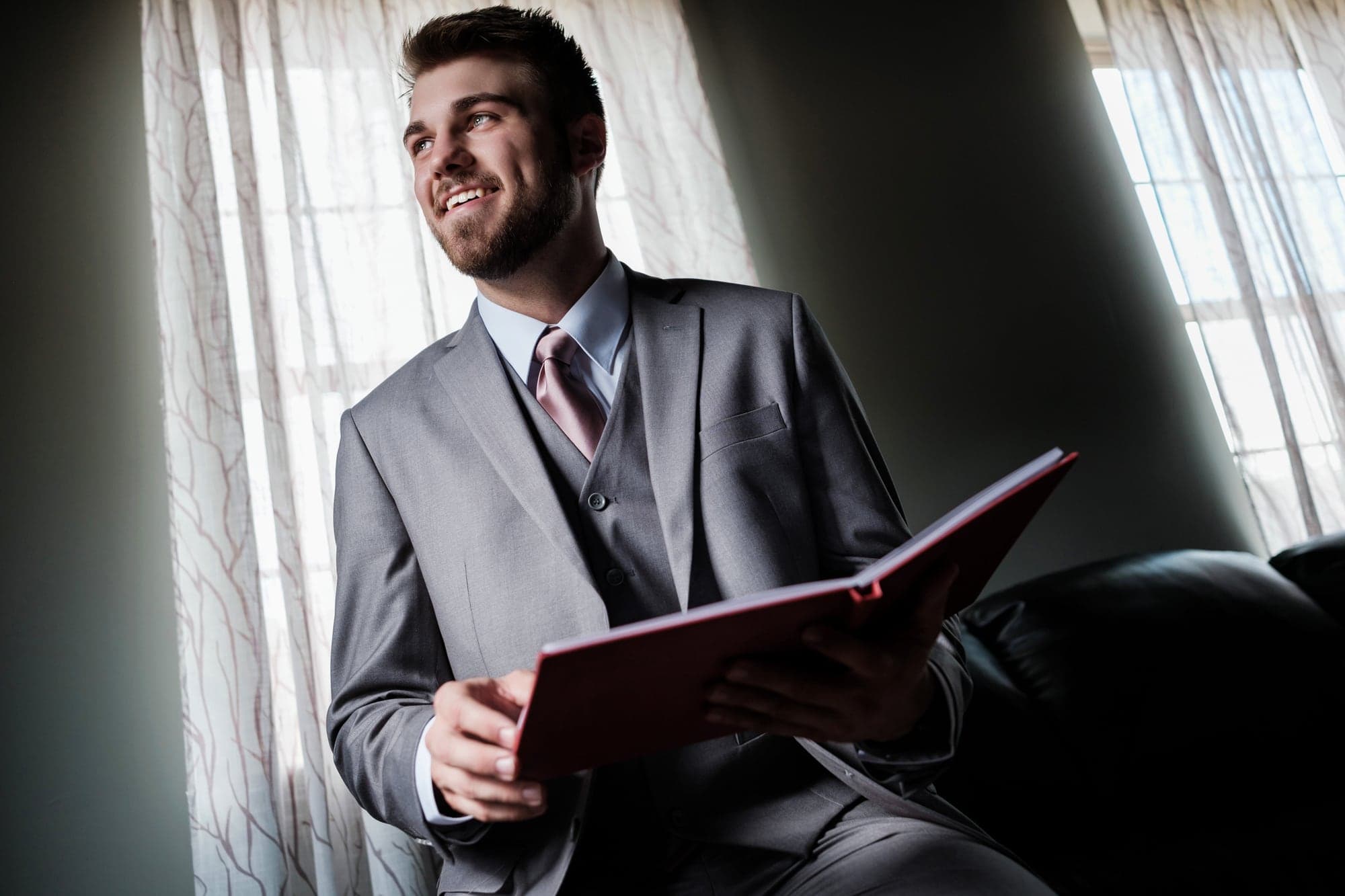 Joshua preparing in a gray suit beside a window at Fiddle Dee Farms