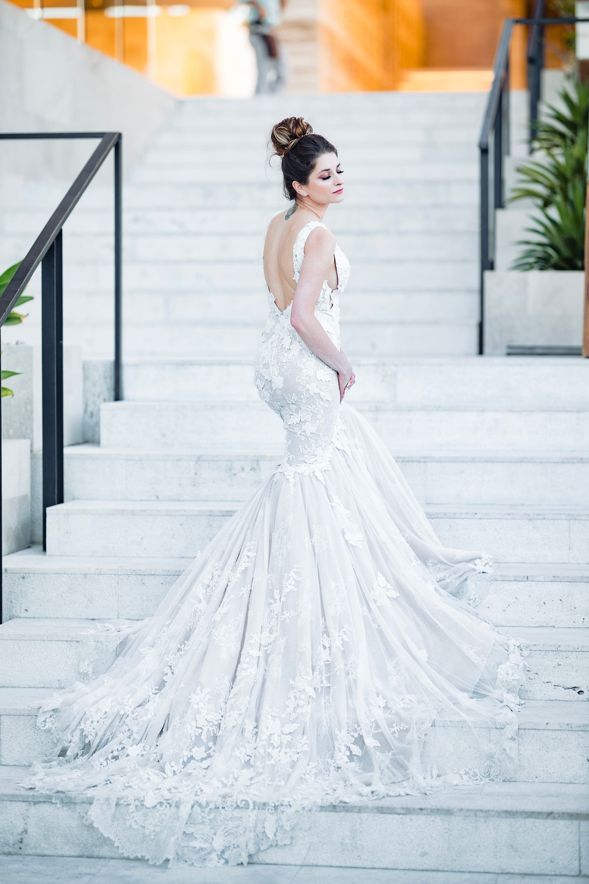 A bride on a pale stone staircase, her train falling down the steps behind her.
