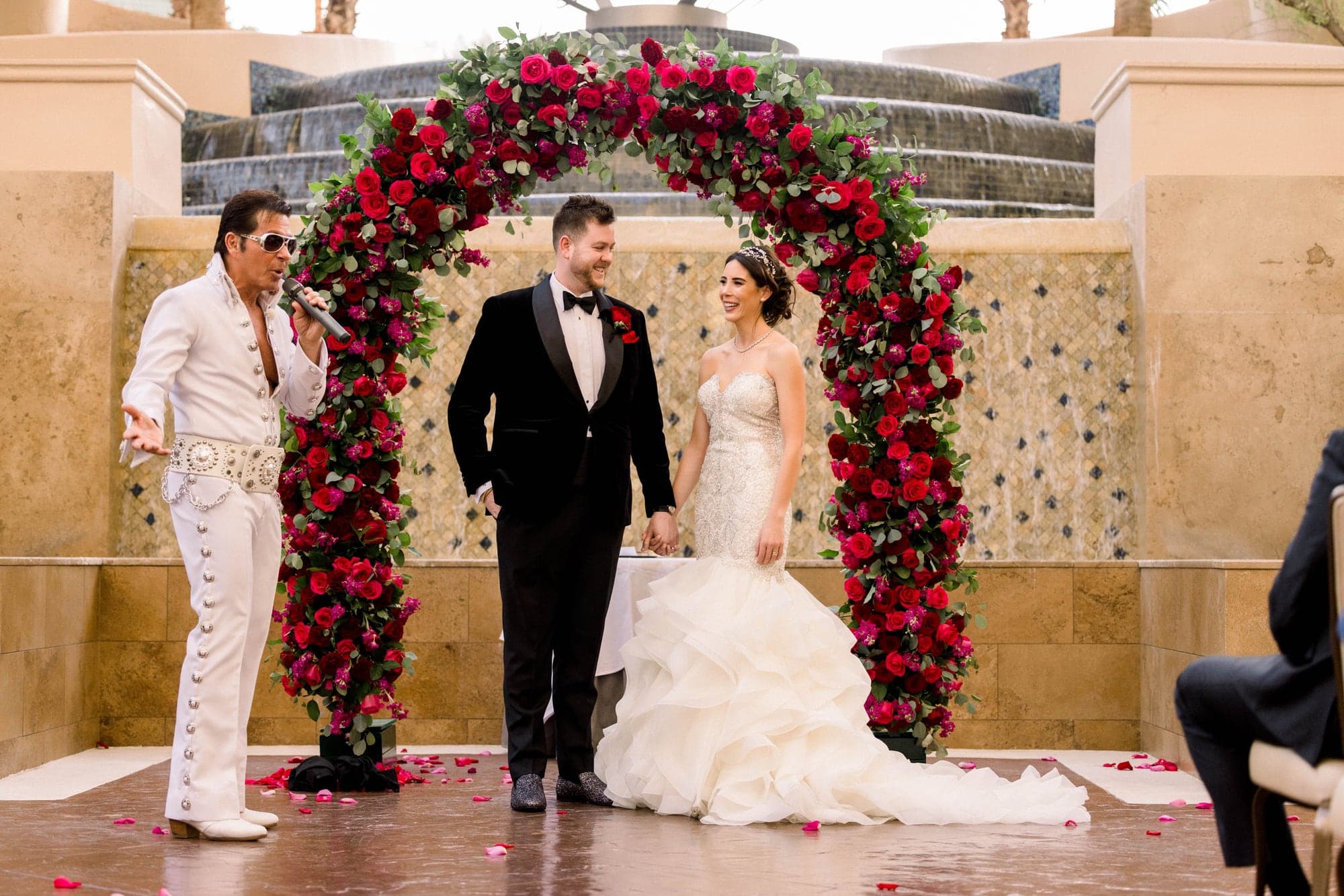Kylie and Jason exchanging vows beneath a red floral arch at Four Seasons Las Vegas
