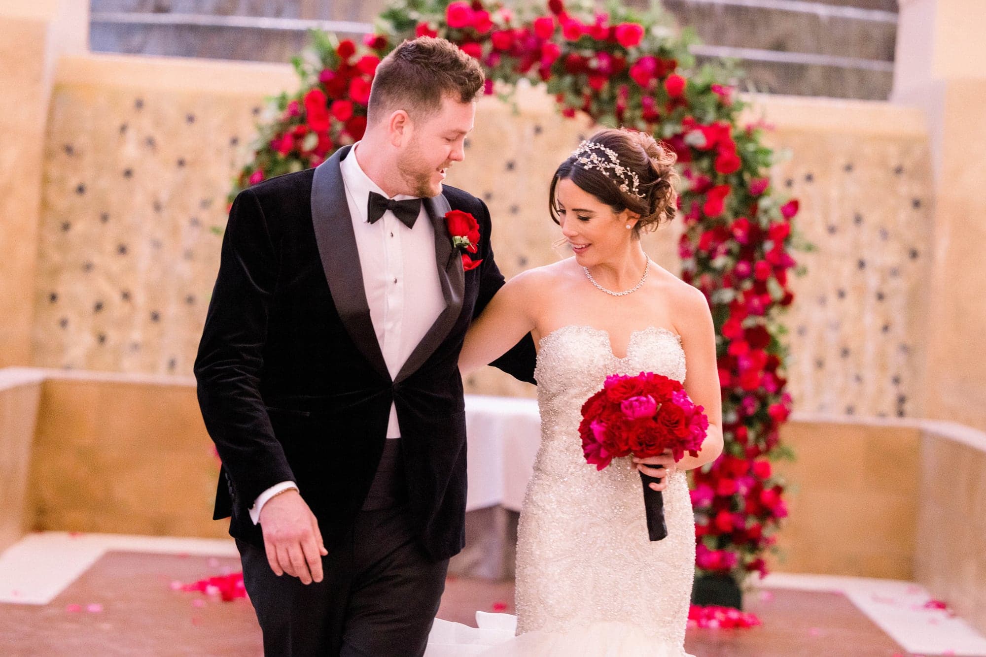 Kylie and Jason standing together beneath the red rose ceremony arch