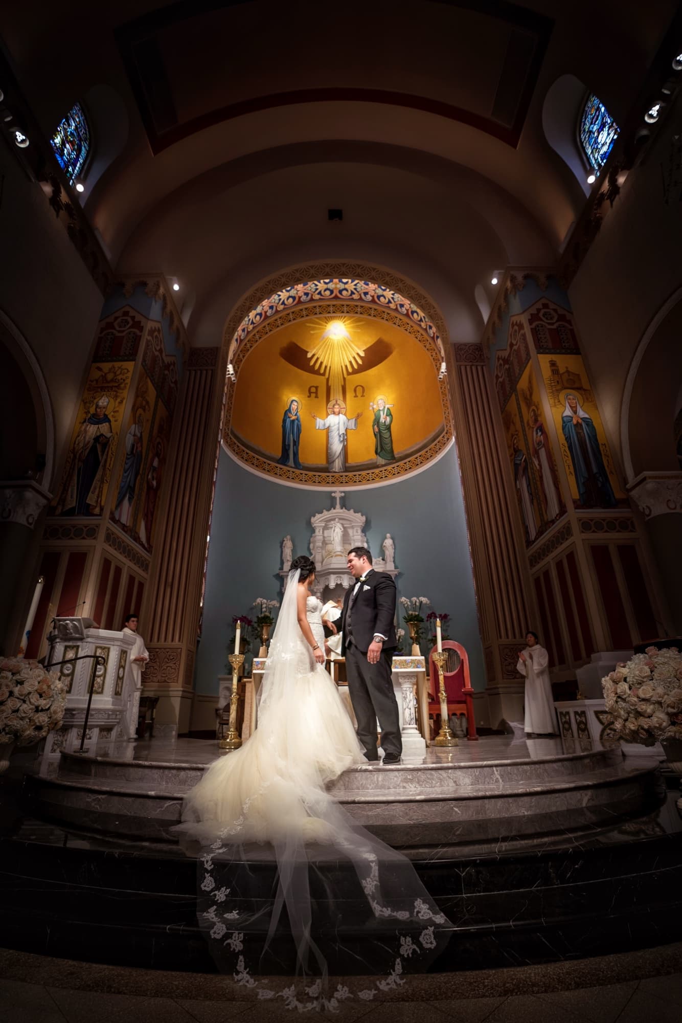 Wide view of the wedding ceremony beneath the golden dome of Saint Monica Catholic Church with the bride's veil pooling down the marble steps