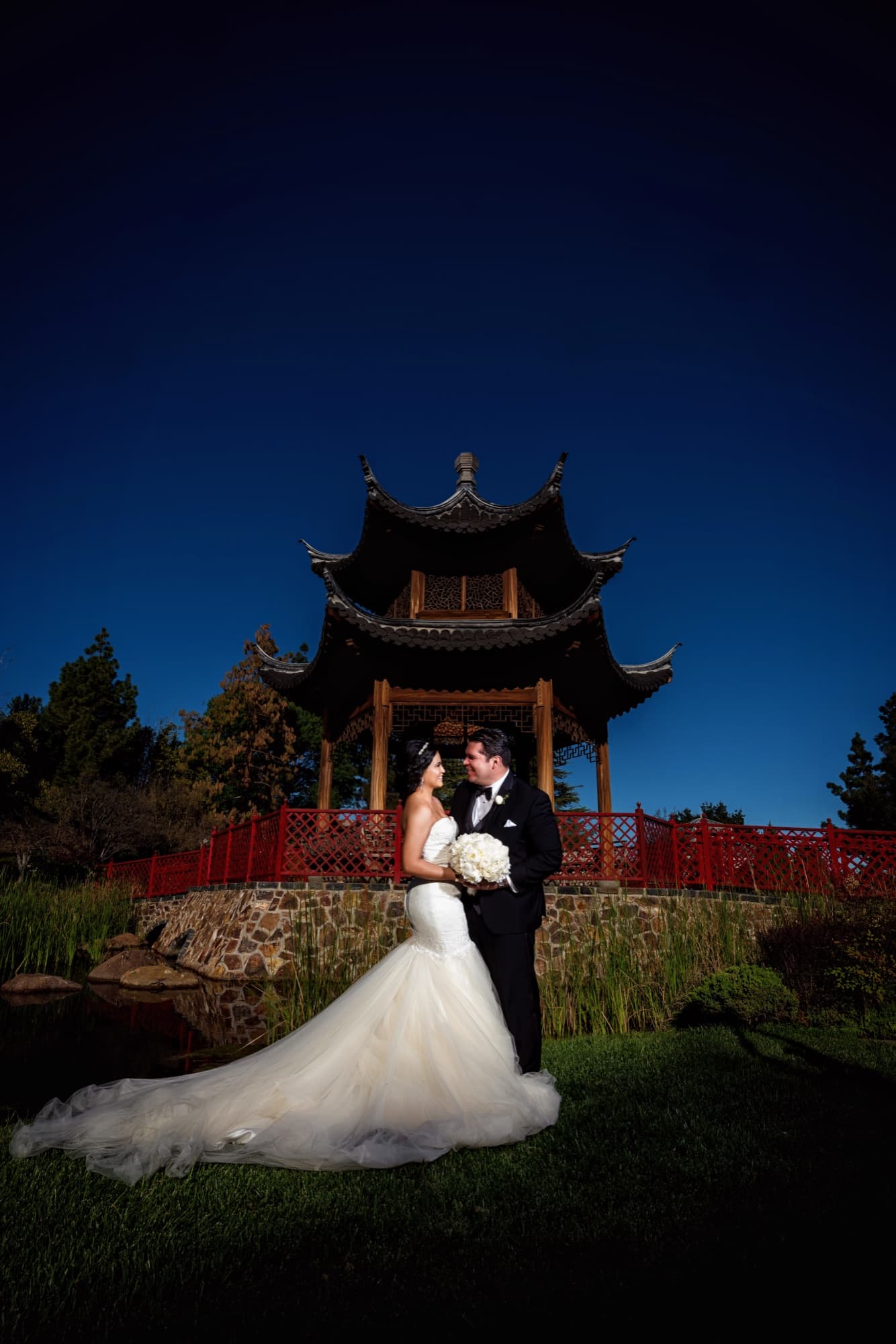 Bride and groom beneath the Chinese pavilion at Gardens of the World in Thousand Oaks against a deep blue dusk sky