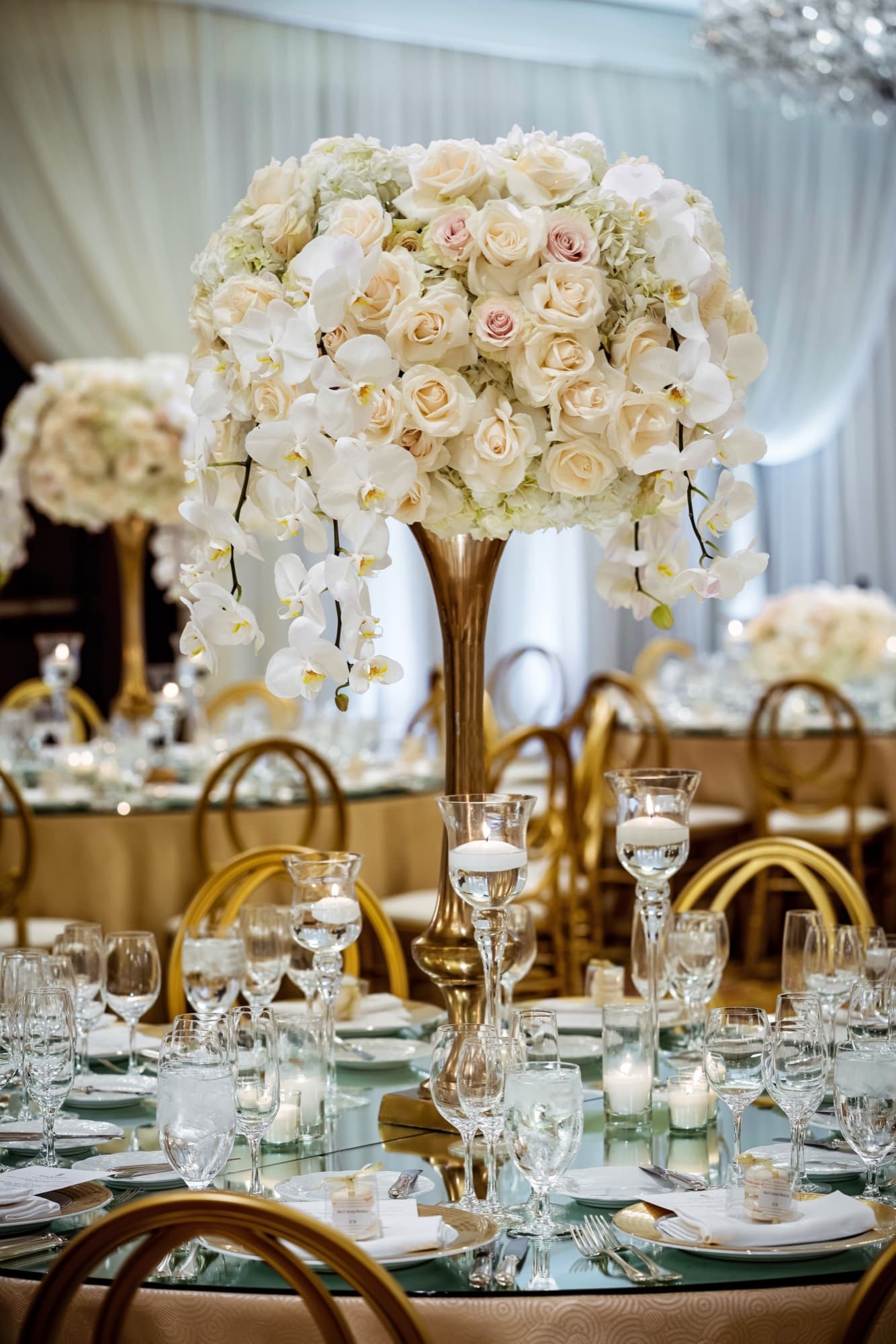 Towering white orchid and blush rose centerpiece over a mirrored table with gold chairs at the Four Seasons Westlake Village wedding reception