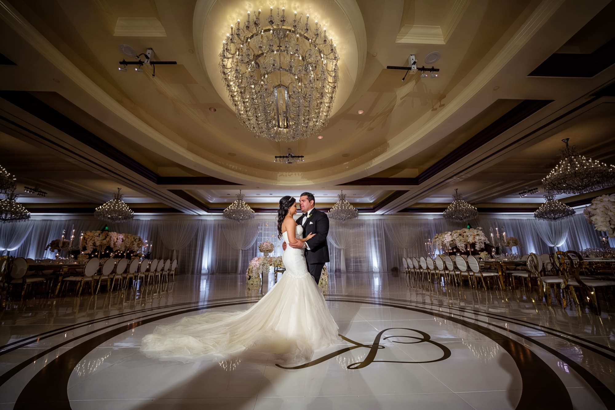 Kyrene and Julio embracing alone on the monogrammed dance floor of the Four Seasons Westlake Village ballroom beneath crystal chandeliers