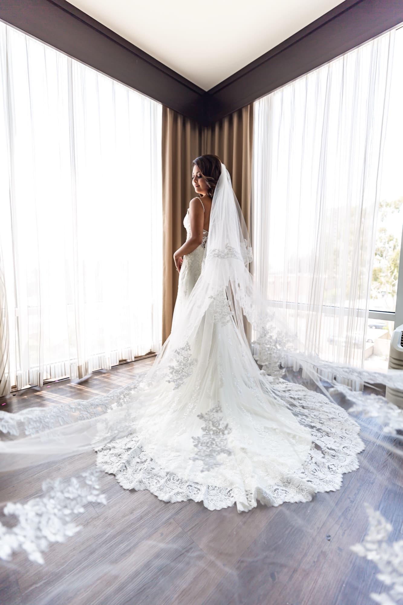 Angela standing at the hotel window in her gown, her lace cathedral train sweeping across the floor behind her