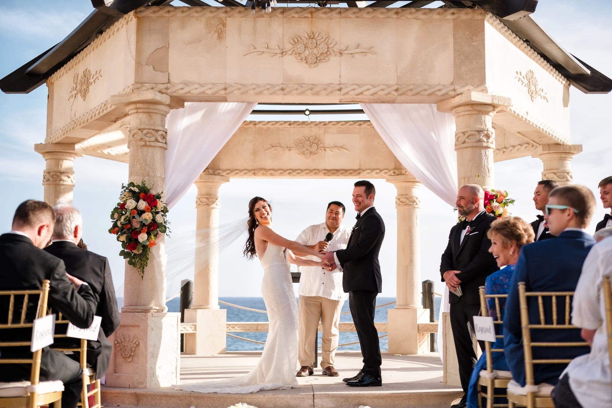 Tina and David exchanging vows beneath a wooden canopy overlooking the Pacific Ocean