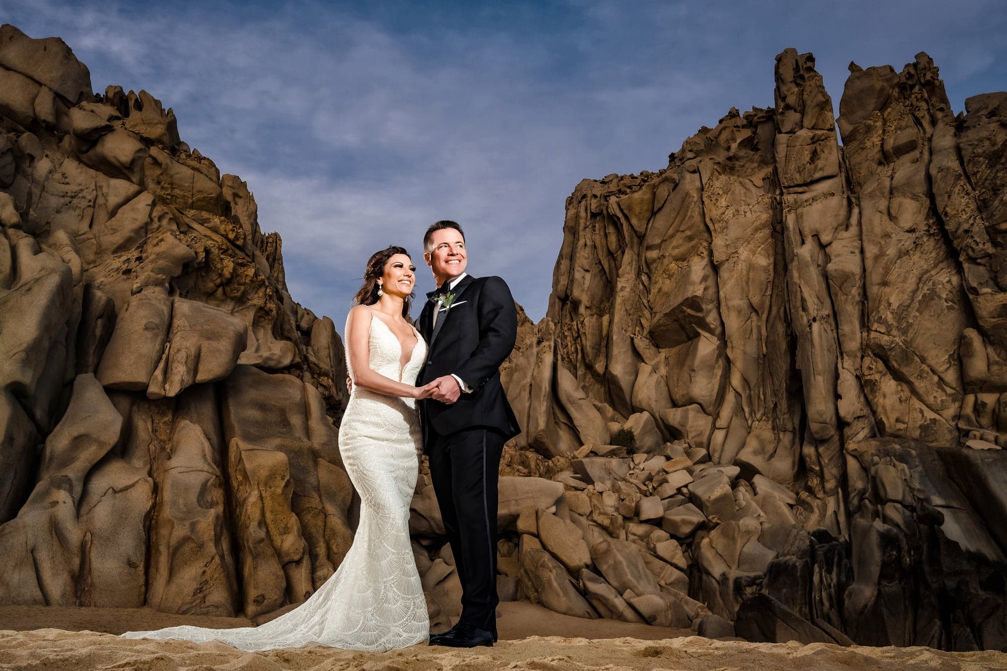 Tina and David embracing among the dramatic coastal rocks at Grand Solmar